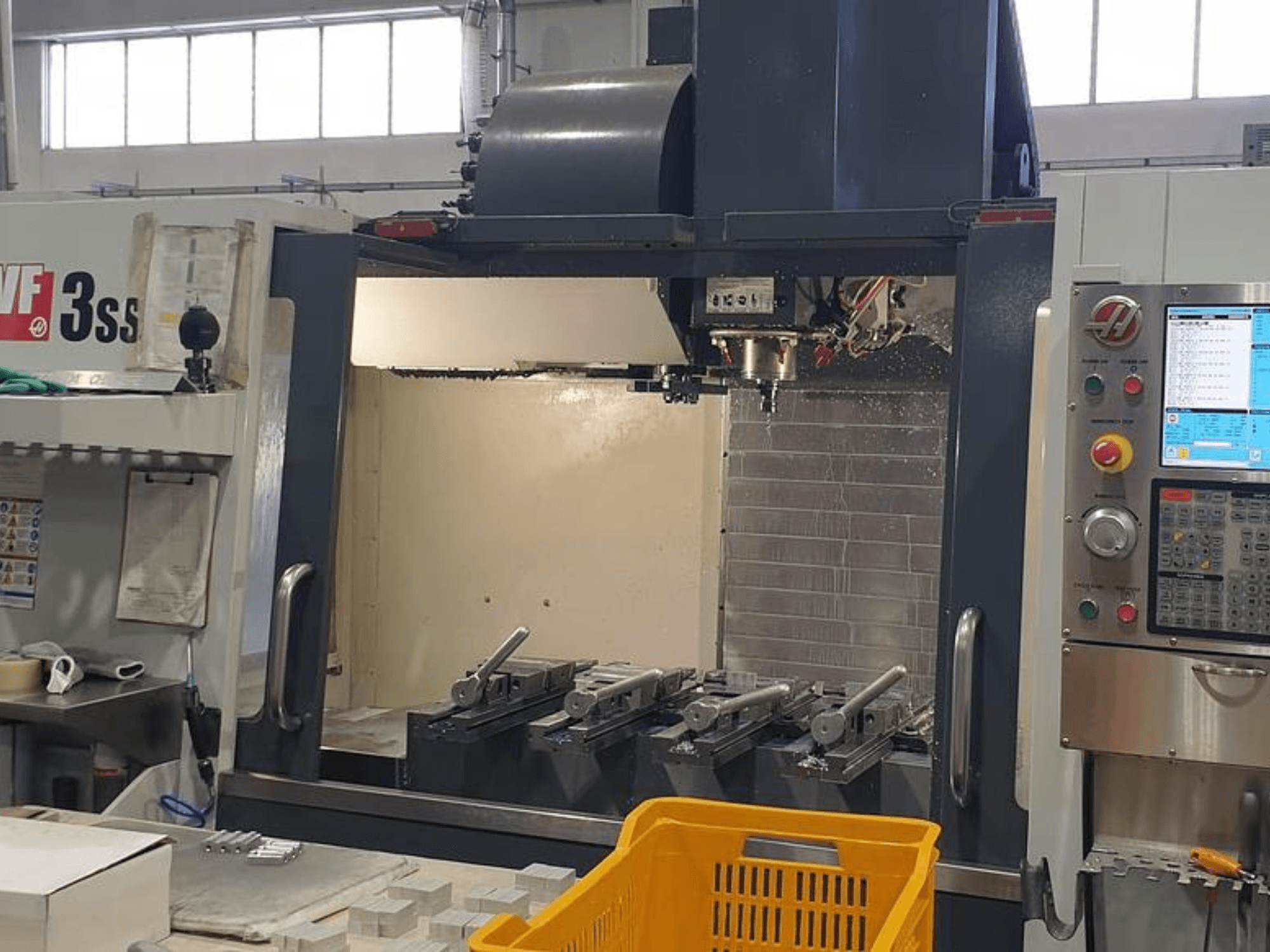 Centro de maquinação vertical HAAS VF-3SS, vista frontal com painel de controlo CNC, ferramentas e cesto laranja.