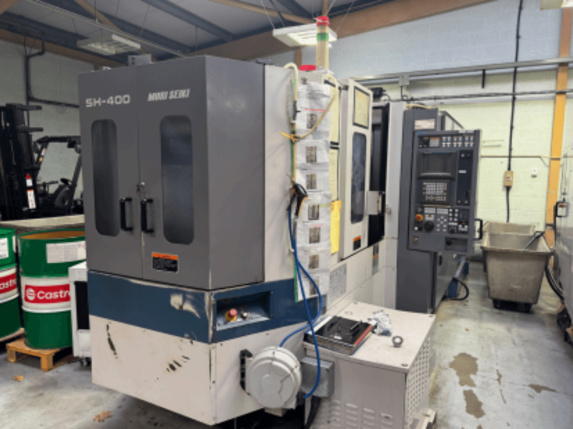Máquina CNC Moni Seiki SH-400, vista lateral mostrando o painel de controlo, as portas e o ambiente industrial circundante.