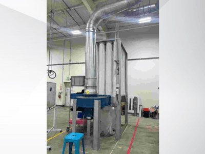 Grande sistema de ventilação industrial, vista frontal, com condutas de metal brilhante e uma base azul, situado num armazém espaçoso.