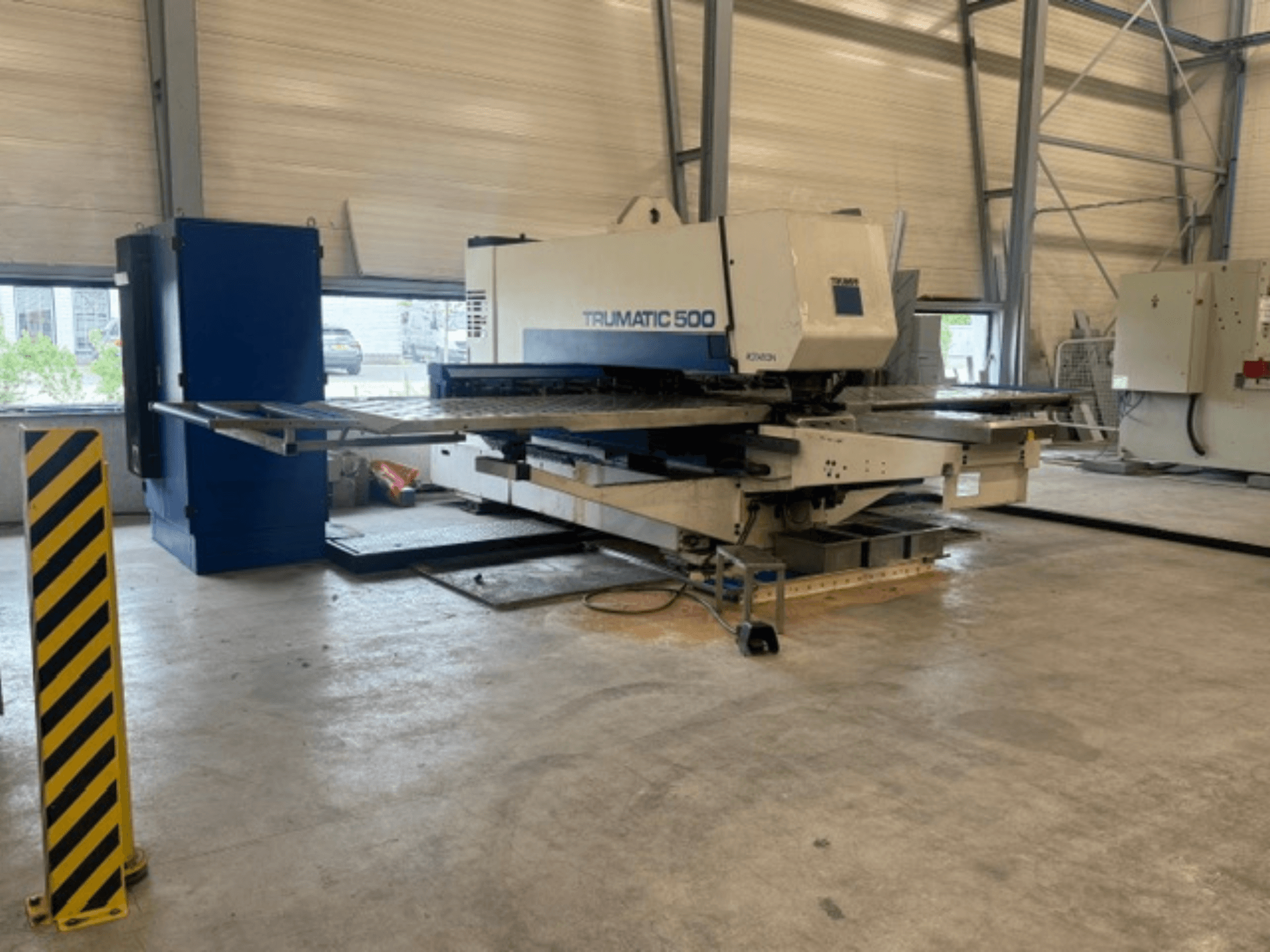 Máquina de perfuração CNC TRUMPF Trumatic 500 numa oficina, vista lateral que mostra a máquina e o poste de segurança com riscas amarelas.