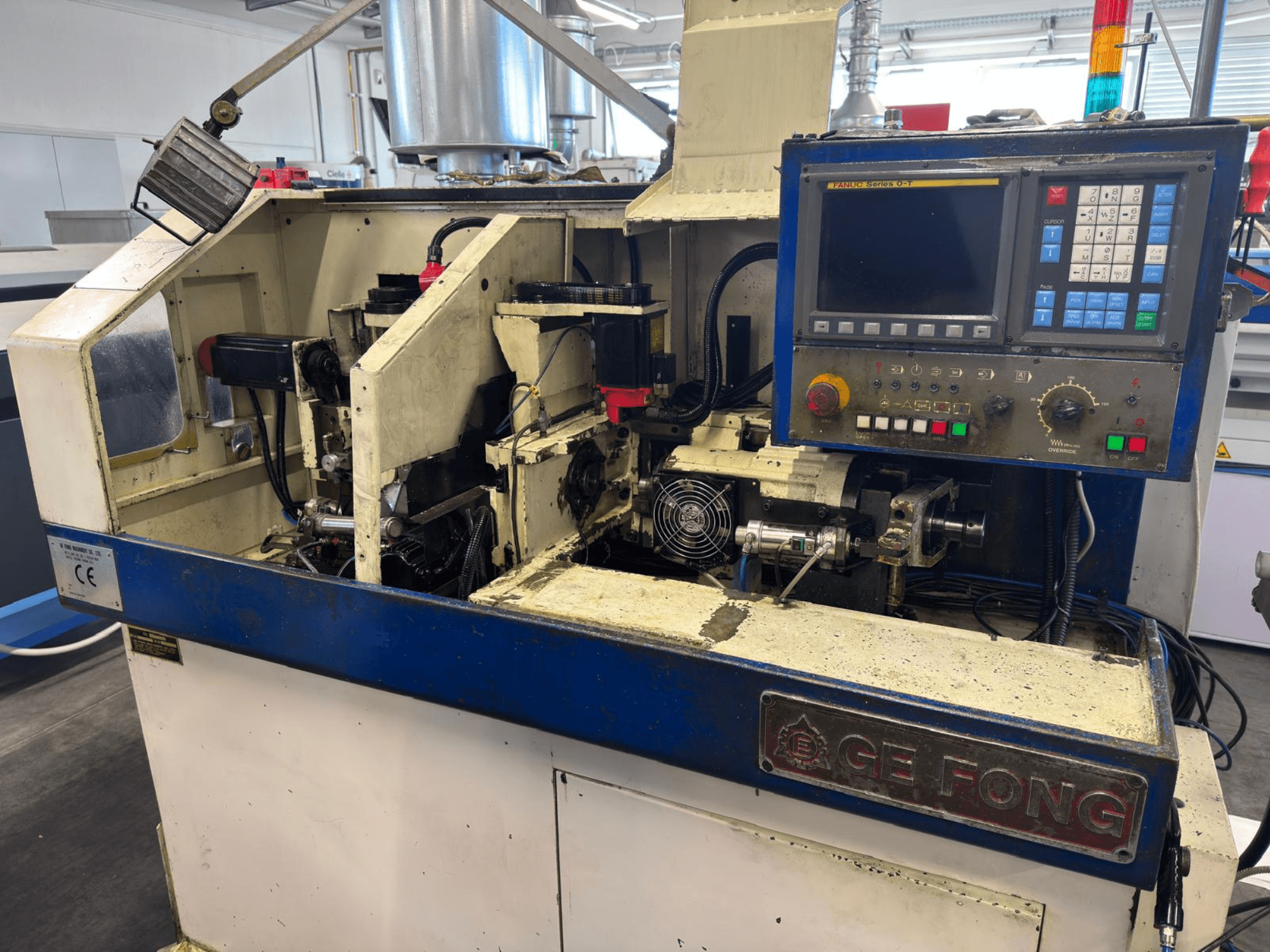 Máquina industrial GE FONG em vista frontal, mostrando componentes internos, painel de controlo e peças operacionais.