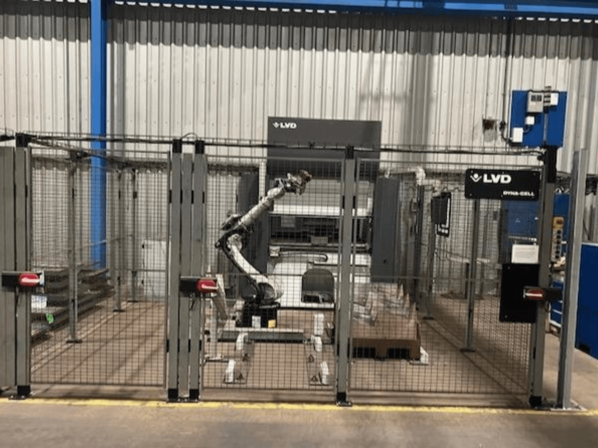 Estação de trabalho robótica LVD Dyna-Cell num recinto vedado, vista frontal, com braço robótico e painel de controlo.