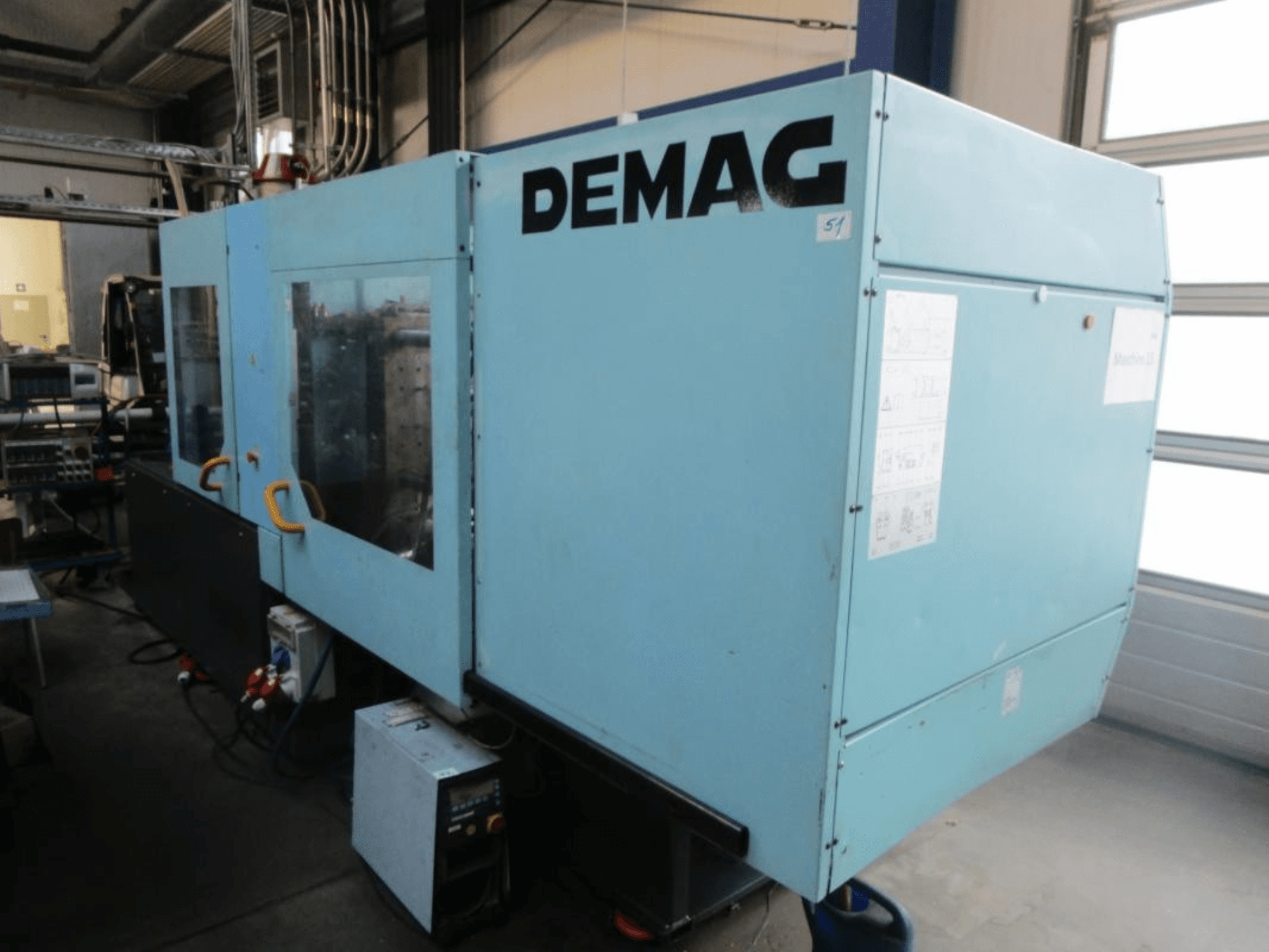 Vista frontal de uma máquina de moldagem por injeção hidráulica DEMAG Ergotech 150-610 Viva, com o painel de controlo e as alavancas visíveis.