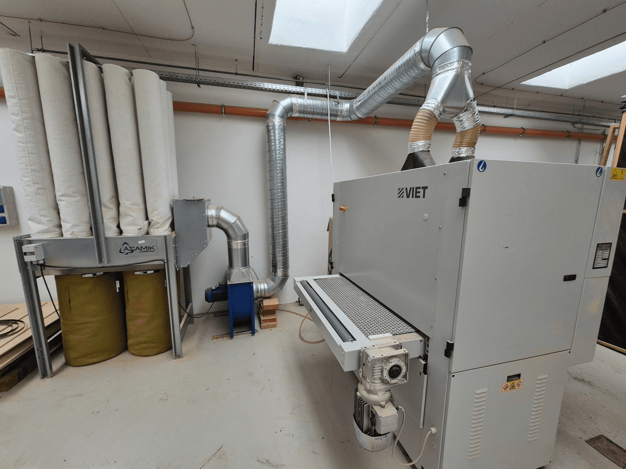 Sistema de extração de poeiras do Viet com filtros cilíndricos e um exaustor prateado, visto de frente numa oficina.