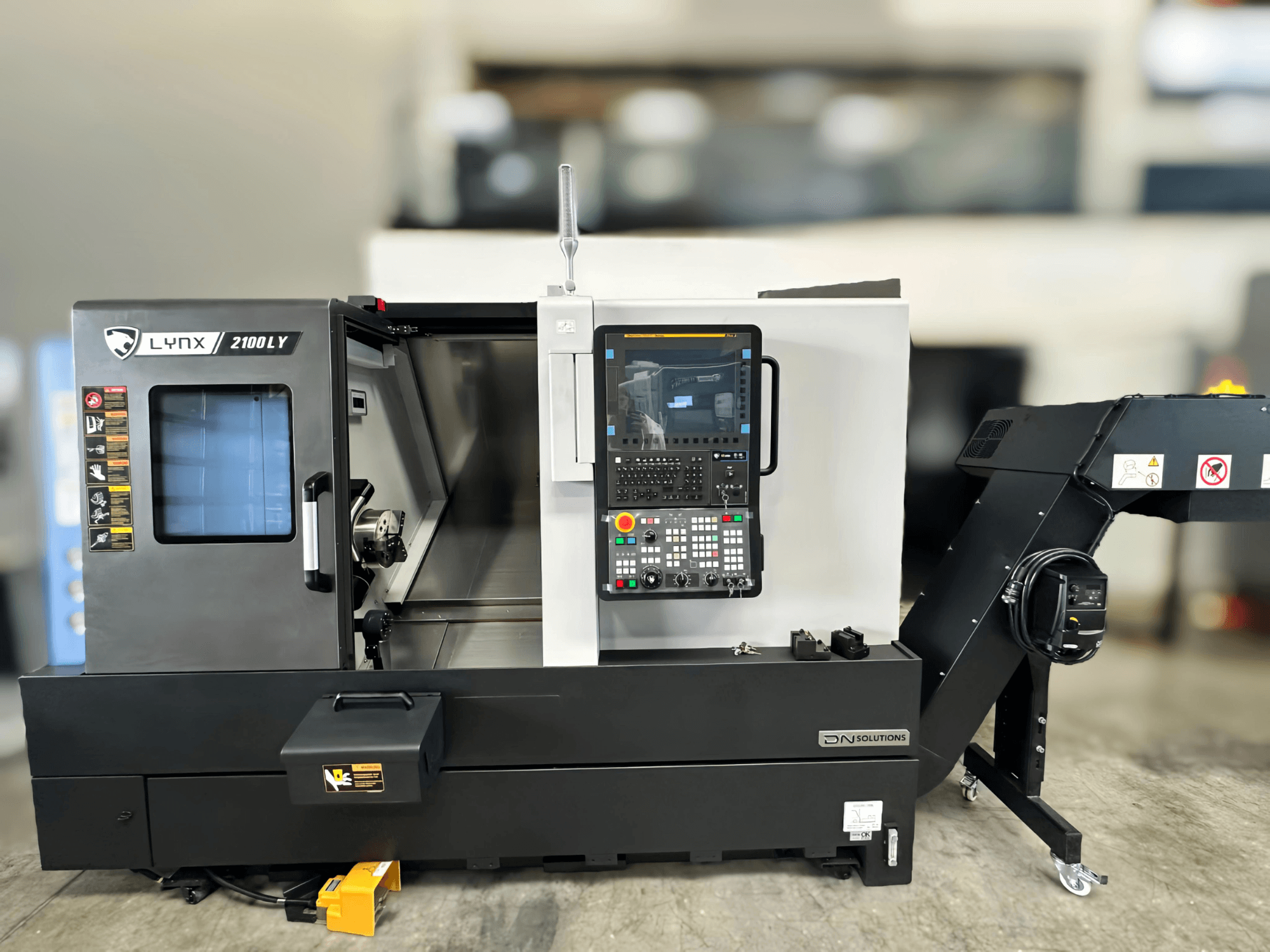 Torneiro horizontal DN SOLUTIONS LYNX 2100LYB, vista frontal, com painel de controlo e porta aberta que revela o interior.