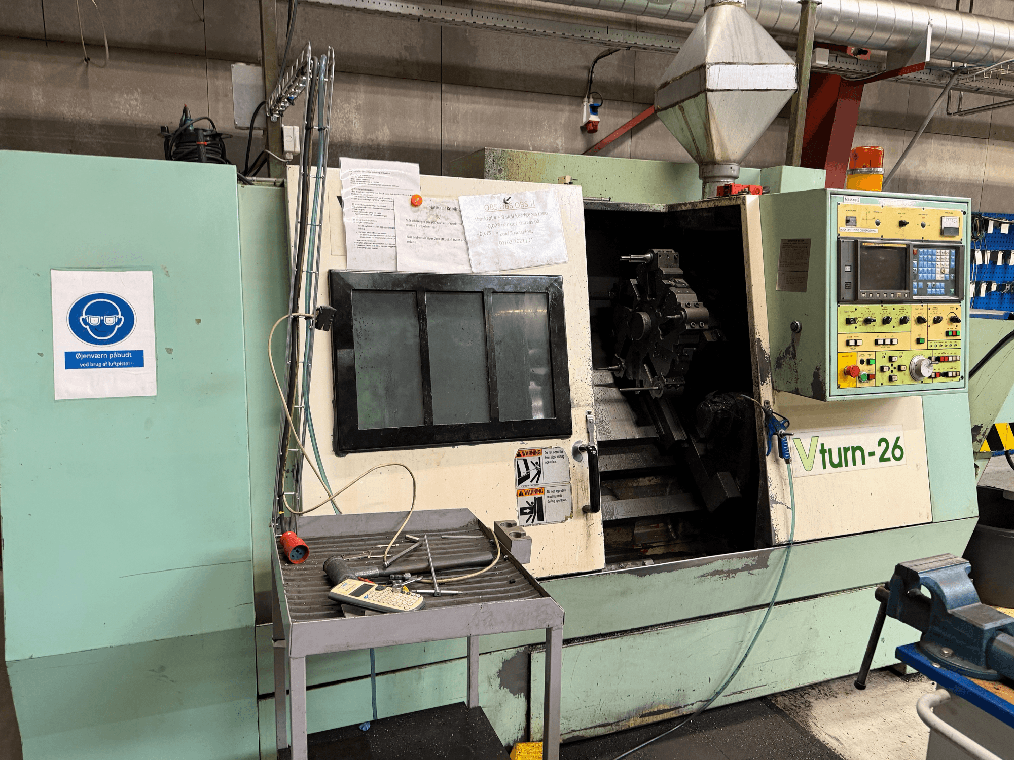 Vista frontal da máquina de torneamento horizontal VICTORY VTurn-26, com o painel de controlo, a área de trabalho e a sinalização de segurança visíveis.