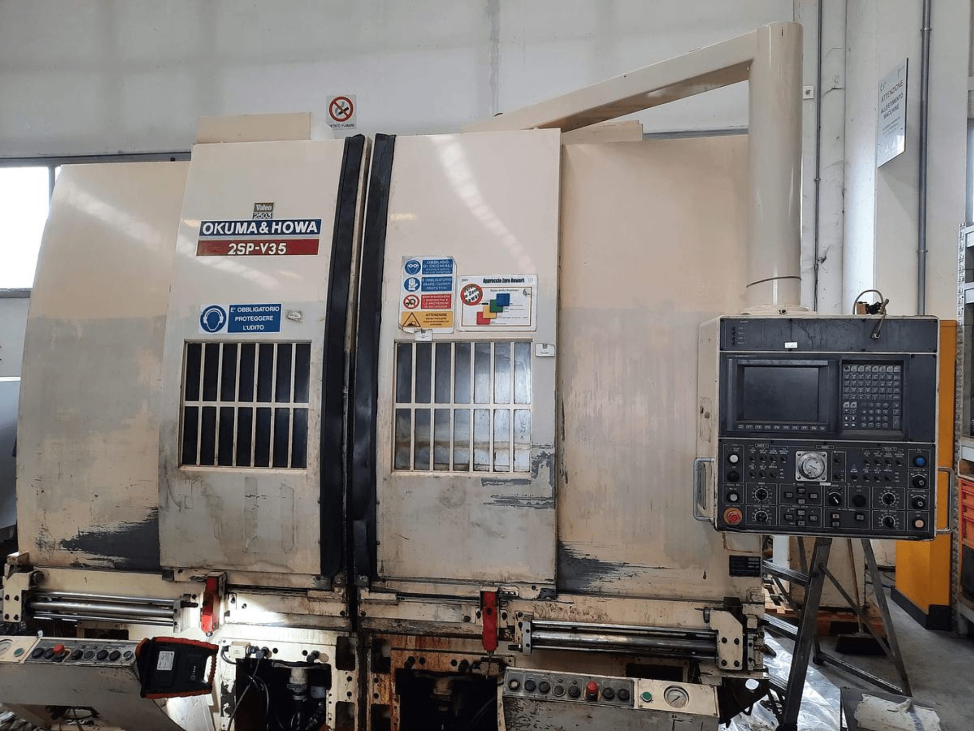 Máquina CNC OKUMA & HOWA 2SP-V35 vista de frente, com painel de controlo com vários botões e etiquetas de segurança.