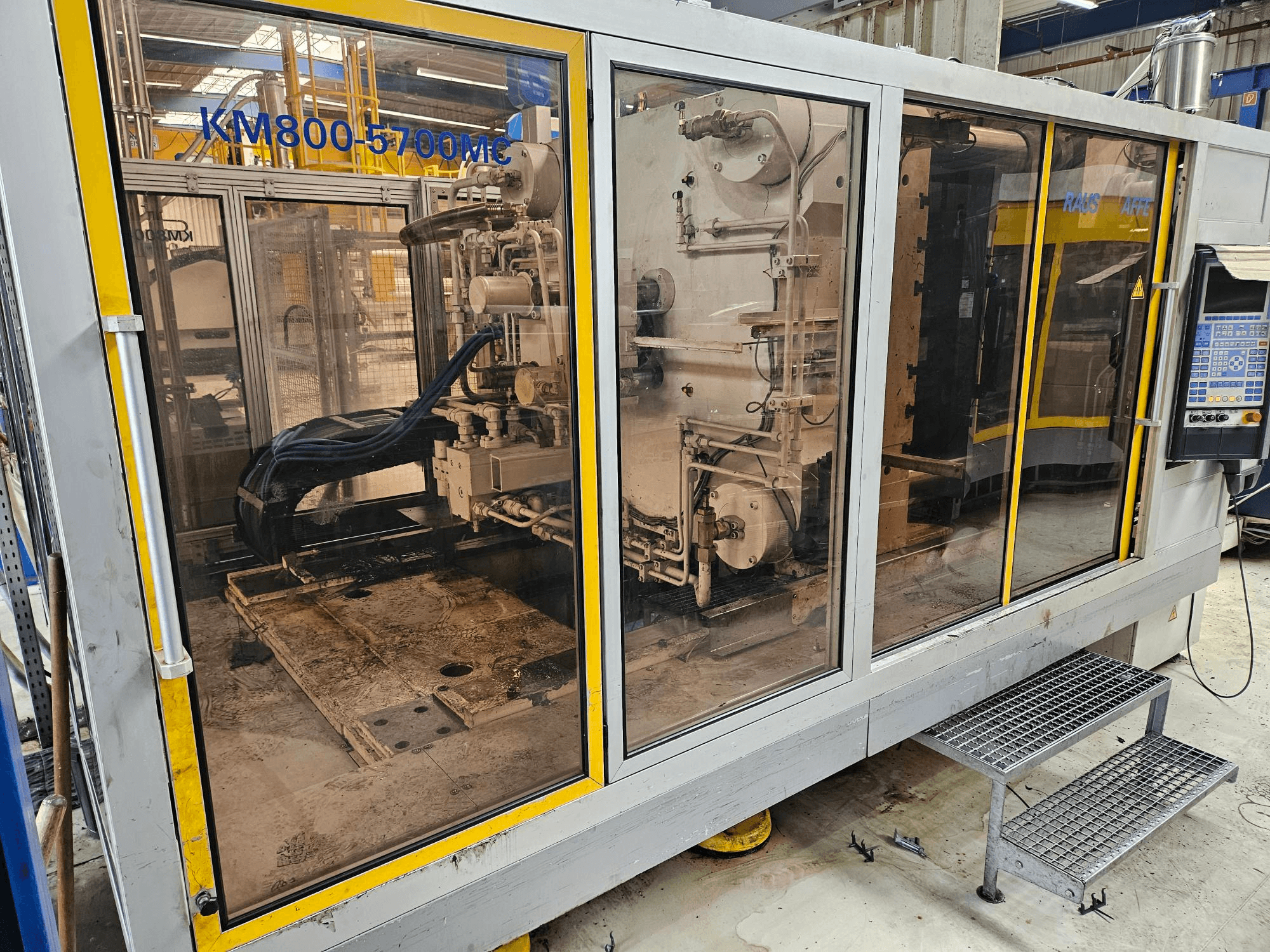 Máquina de moldagem por injeção hidráulica Krauss Maffei KM800-5700 MC, vista frontal que mostra os componentes através de painéis de vidro.