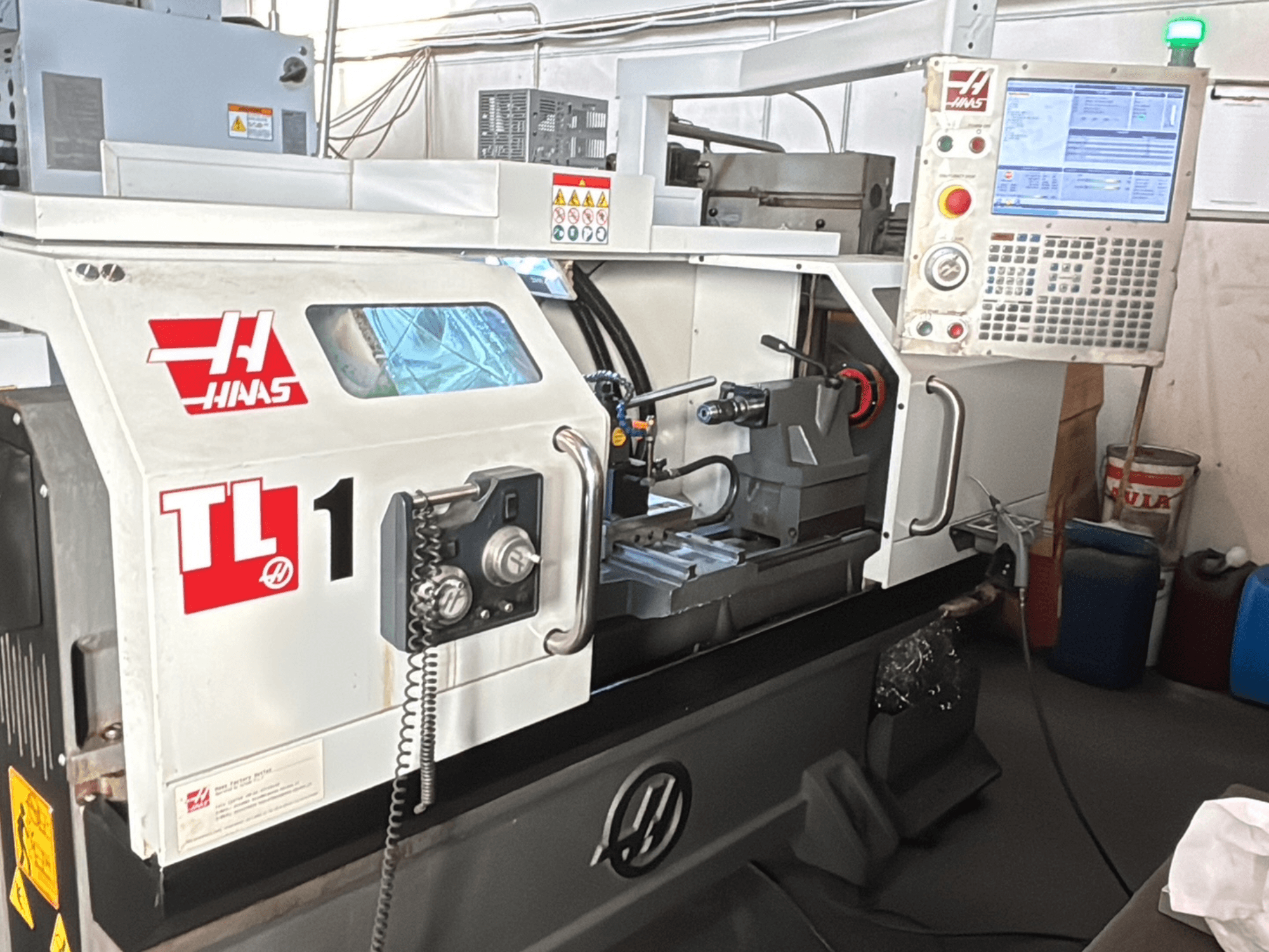 Torno CNC Haas TL-1, vista frontal, apresenta painel de controlo com visor, suporte de ferramentas e etiquetas de segurança.