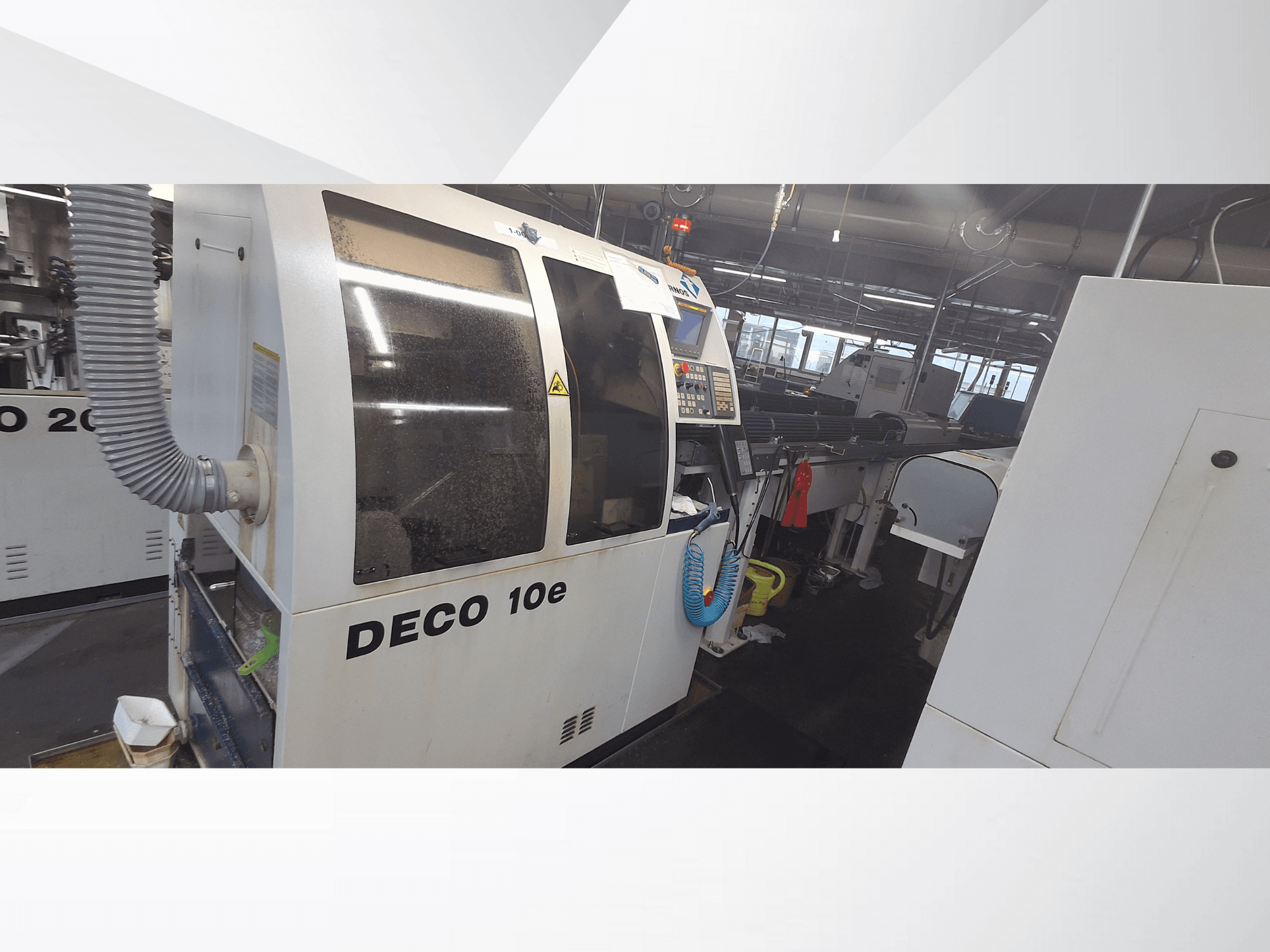 Máquina DECO 10e numa oficina; vista lateral mostrando o painel de controlo e a mangueira de ventilação, com máquinas desfocadas ao fundo.