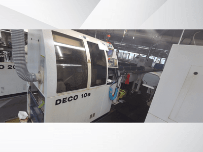 Máquina DECO 10e numa oficina; vista lateral mostrando o painel de controlo e a mangueira de ventilação, com máquinas desfocadas ao fundo.