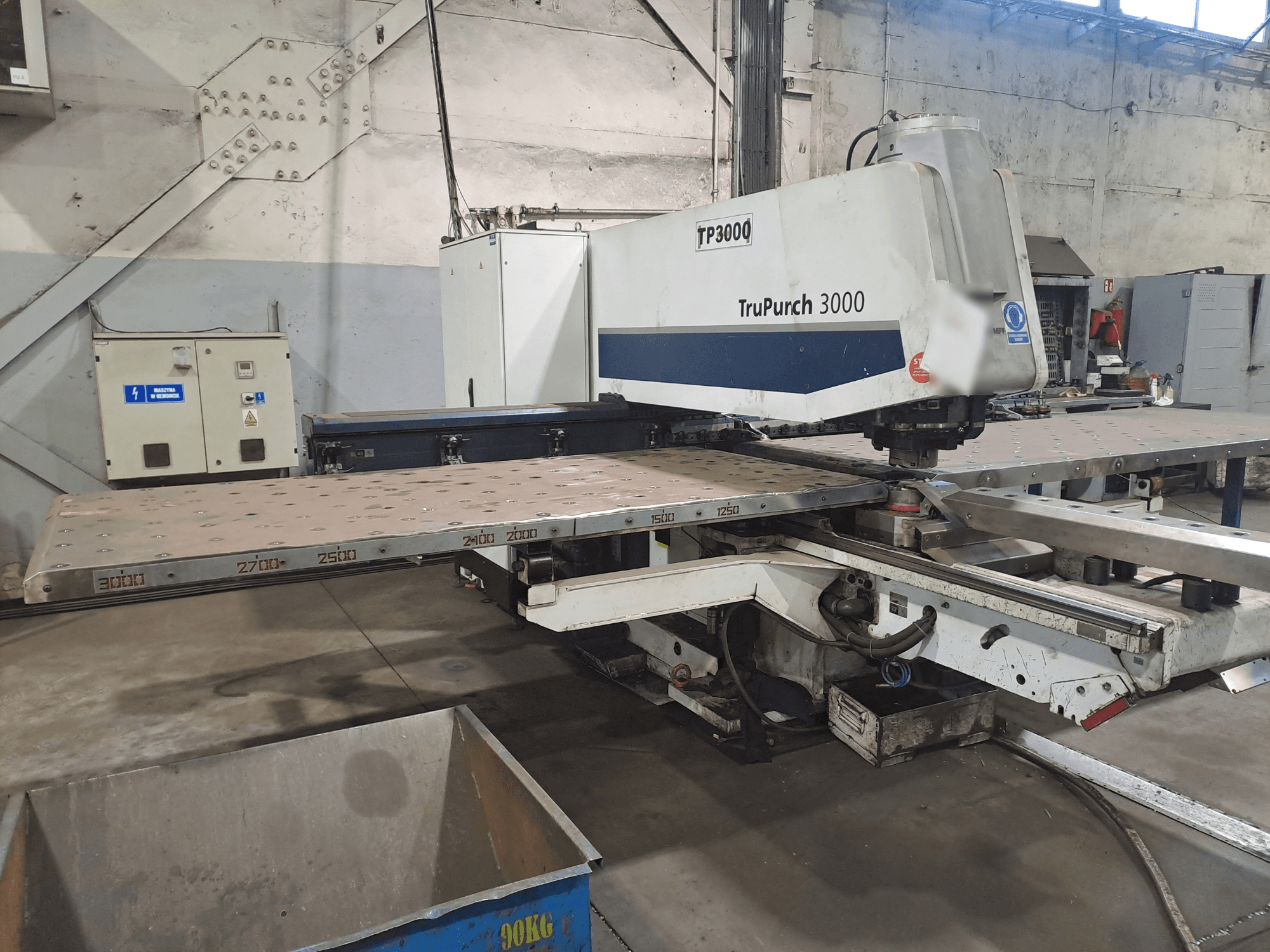 Máquina CNC TruPunch 3000 mostrada de frente, com uma grande placa de metal e marcações de medição, num ambiente industrial.