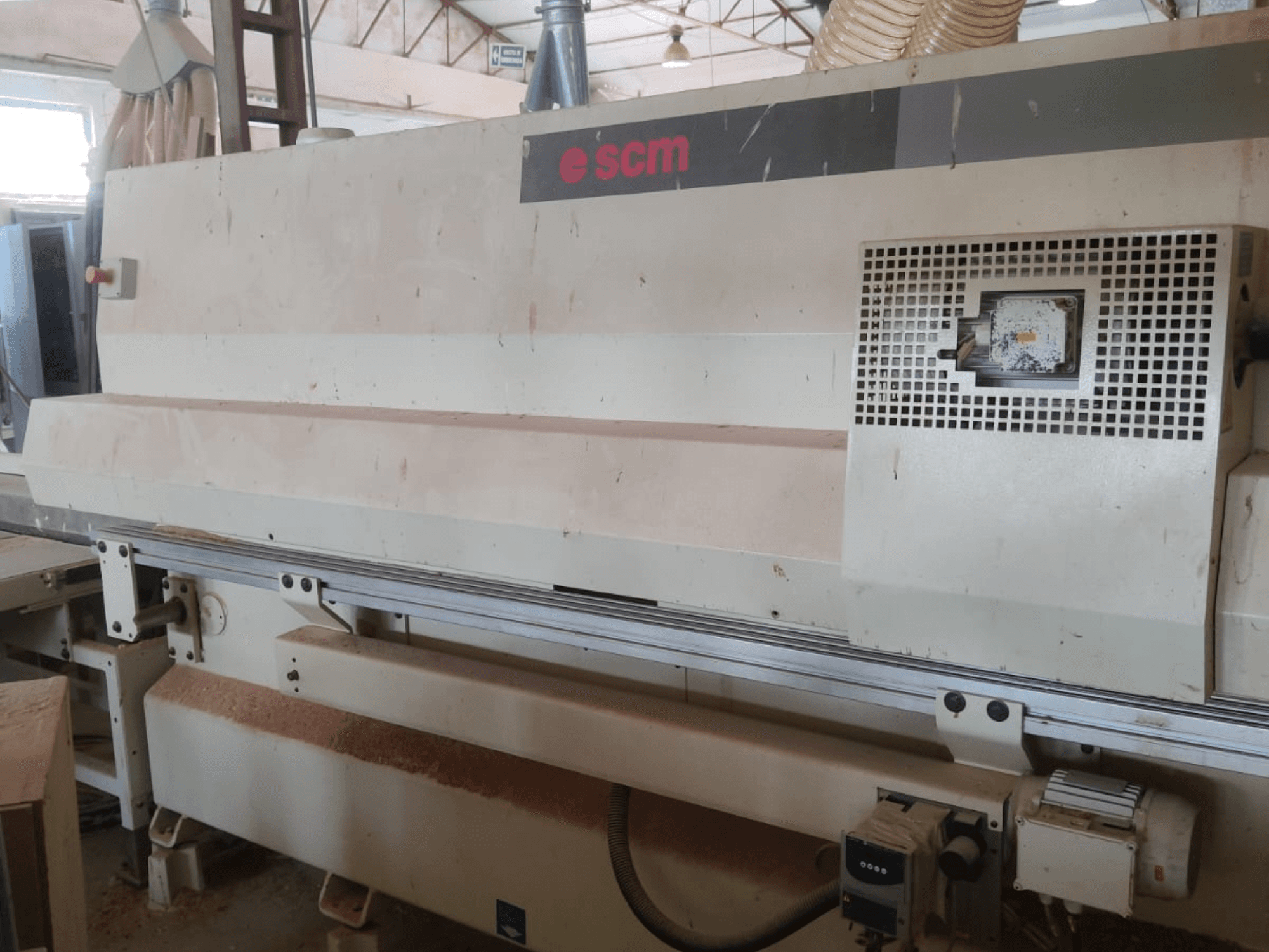 Centro de usinagem de madeira CNC SCM Windor60, vista frontal. Mostra os comandos da máquina e o sistema de recolha de pó, com aparas de madeira por baixo.