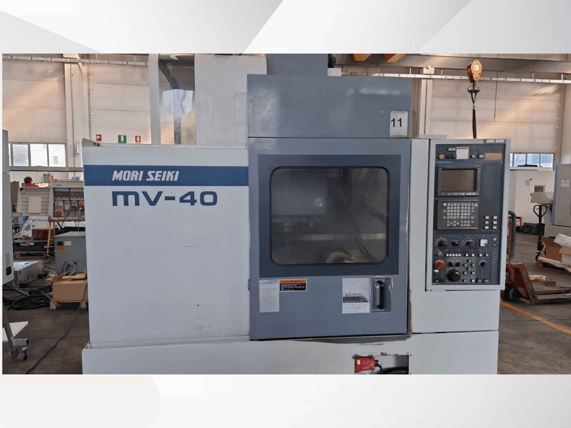 Centro de maquinação vertical MORI SEIKI MV-40, vista frontal mostrando o painel de controlo e a janela, numa oficina.