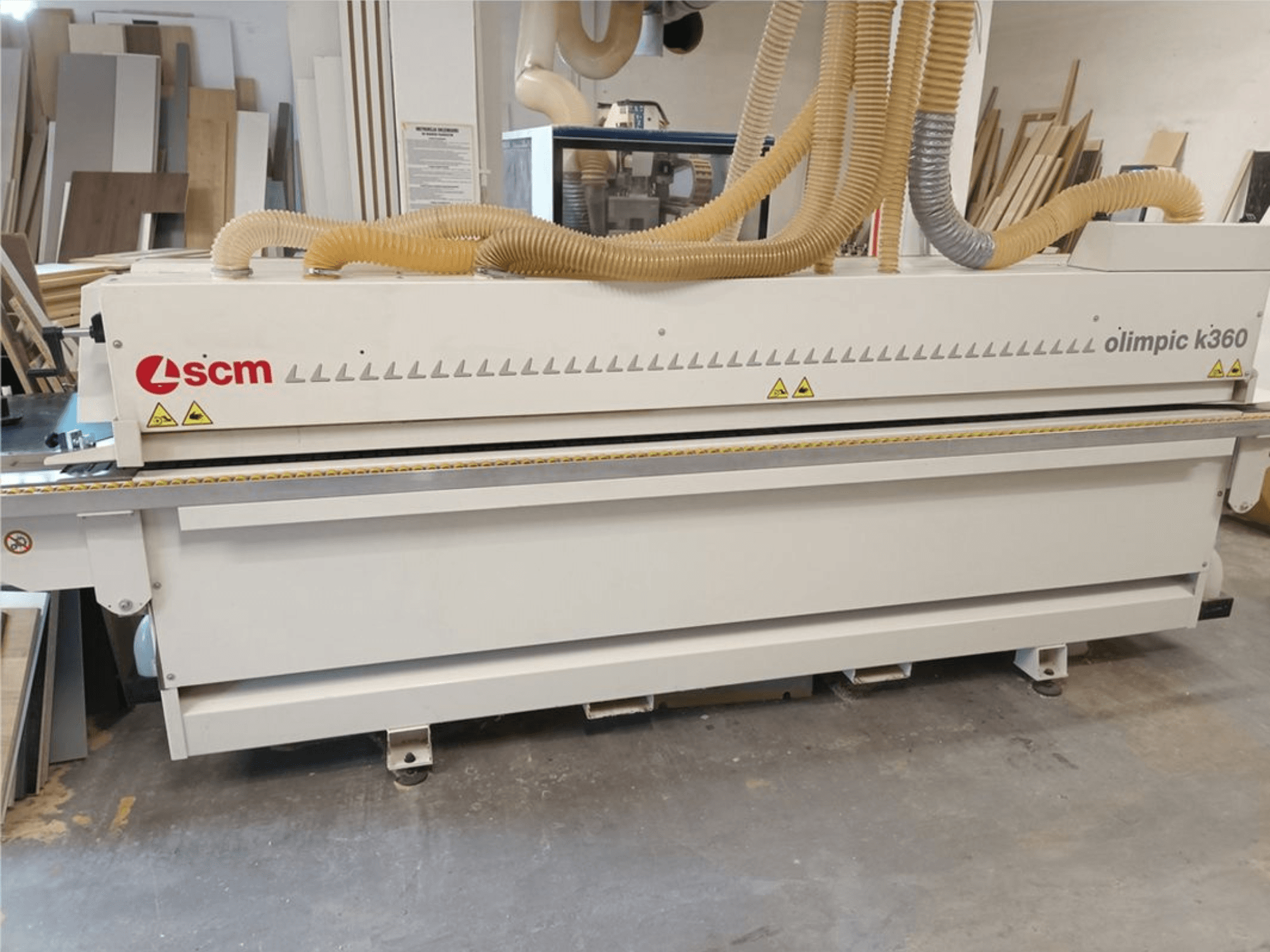 Máquina de colar bordas SCM Olimpic K360 T-ER1 numa oficina, vista frontal que mostra as mangueiras de extração de poeira e as etiquetas de aviso.