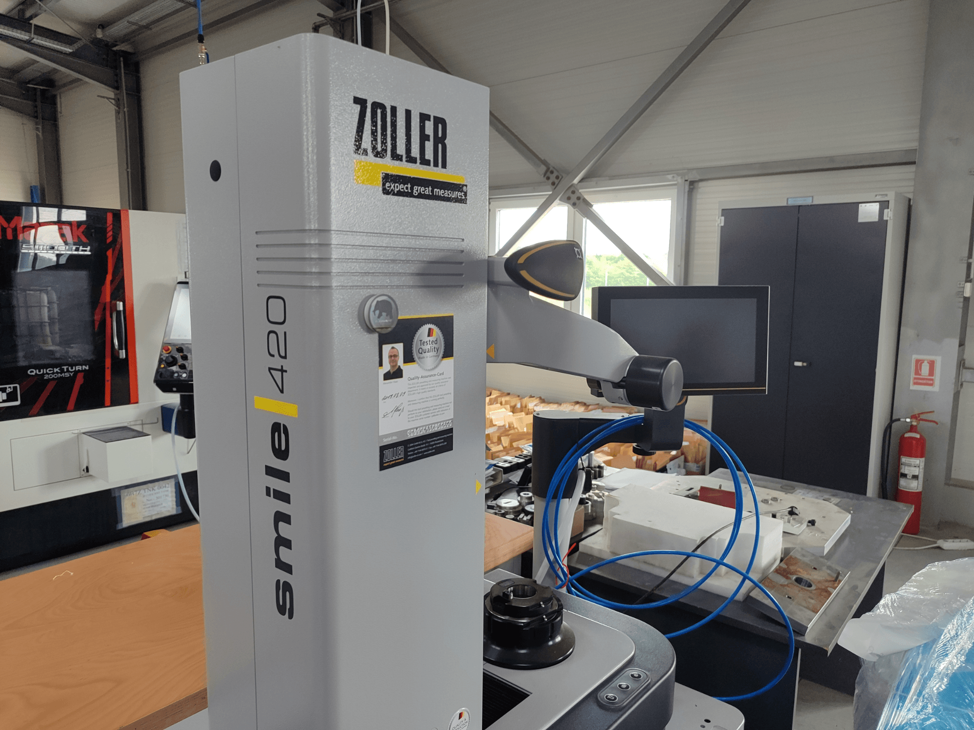 Aparelho de medição ZOLLER smile 420 com monitor, vista lateral numa oficina, com mangueiras azuis e maquinaria em fundo.