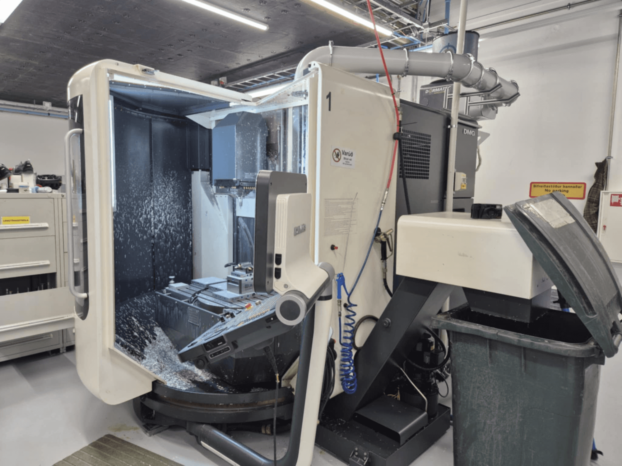 Fresadora DMG aberta com pulverização de líquido de refrigeração, com aparas de metal e comandos de ferramentas, vista de frente.