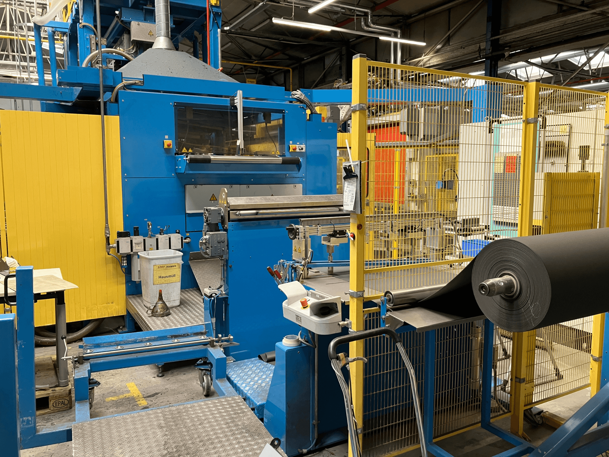 Máquina de processamento de plástico KIEFEL KLS 86/235 vista de frente, com um rolo de material preto e painel de controlo.