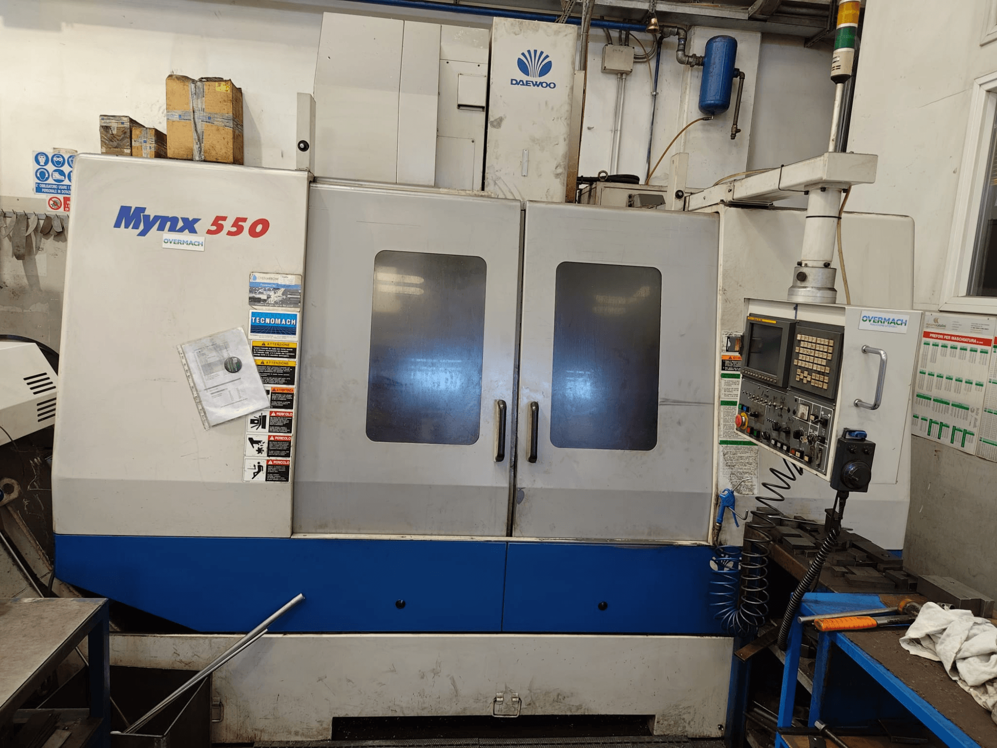 Centro de maquinagem vertical DAEWOO MYNX 550, vista frontal, com painel de controlo, duas portas grandes e etiquetas de segurança.