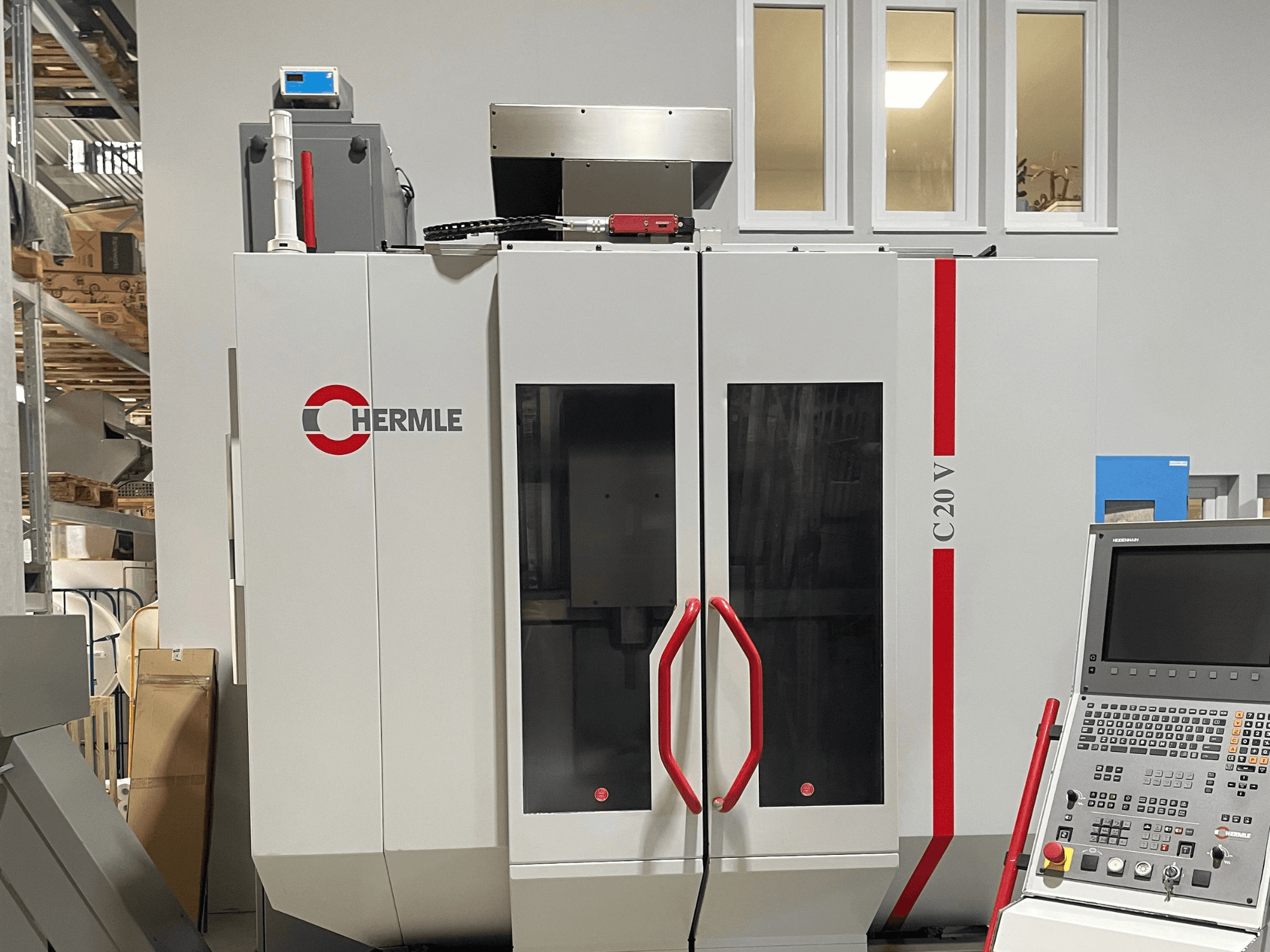 Máquina CNC Chermle C20 V, vista frontal, com painel de controlo e puxadores vermelhos; design industrial com grandes portas de vidro.