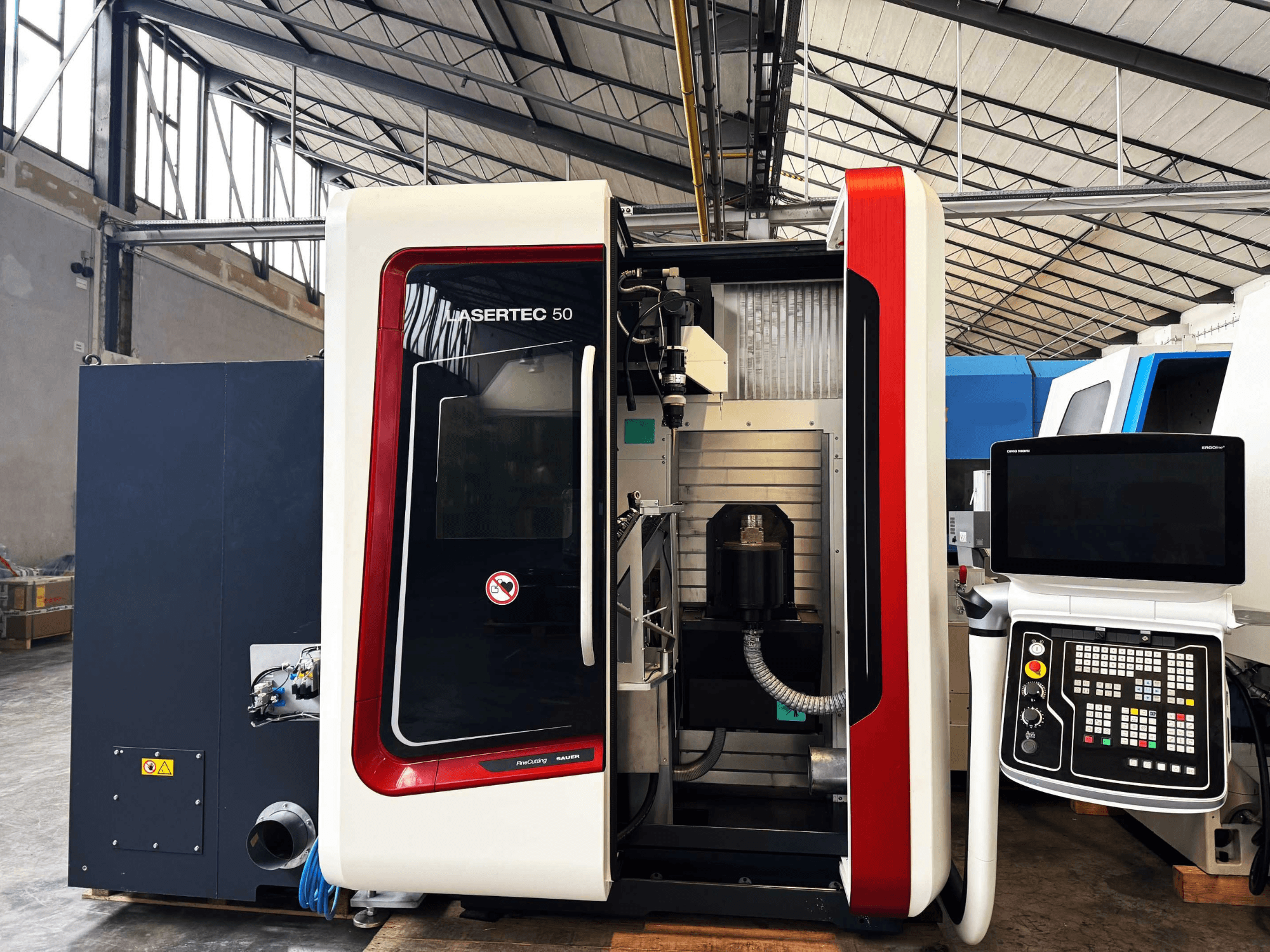 Máquina CNC LaserTec 50 em vista lateral, com painel de controlo a preto e branco, suporte de ferramentas visível e ambiente industrial.
