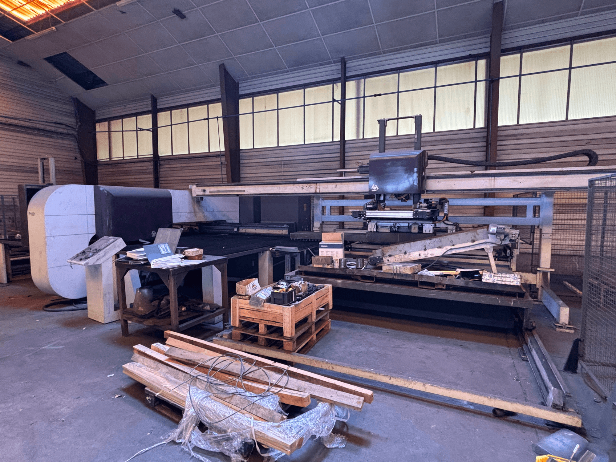Puncionadora CNC DANOBAT P1631 numa oficina, vista de frente, rodeada de materiais e ferramentas num chão desordenado.