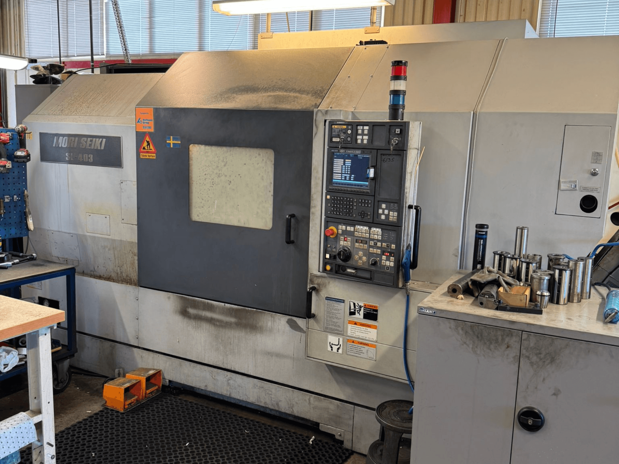 Torneiro horizontal MORI SEIKI SL-403BMC/800 numa oficina, mostrando o painel de controlo e as ferramentas próximas, vista lateral.