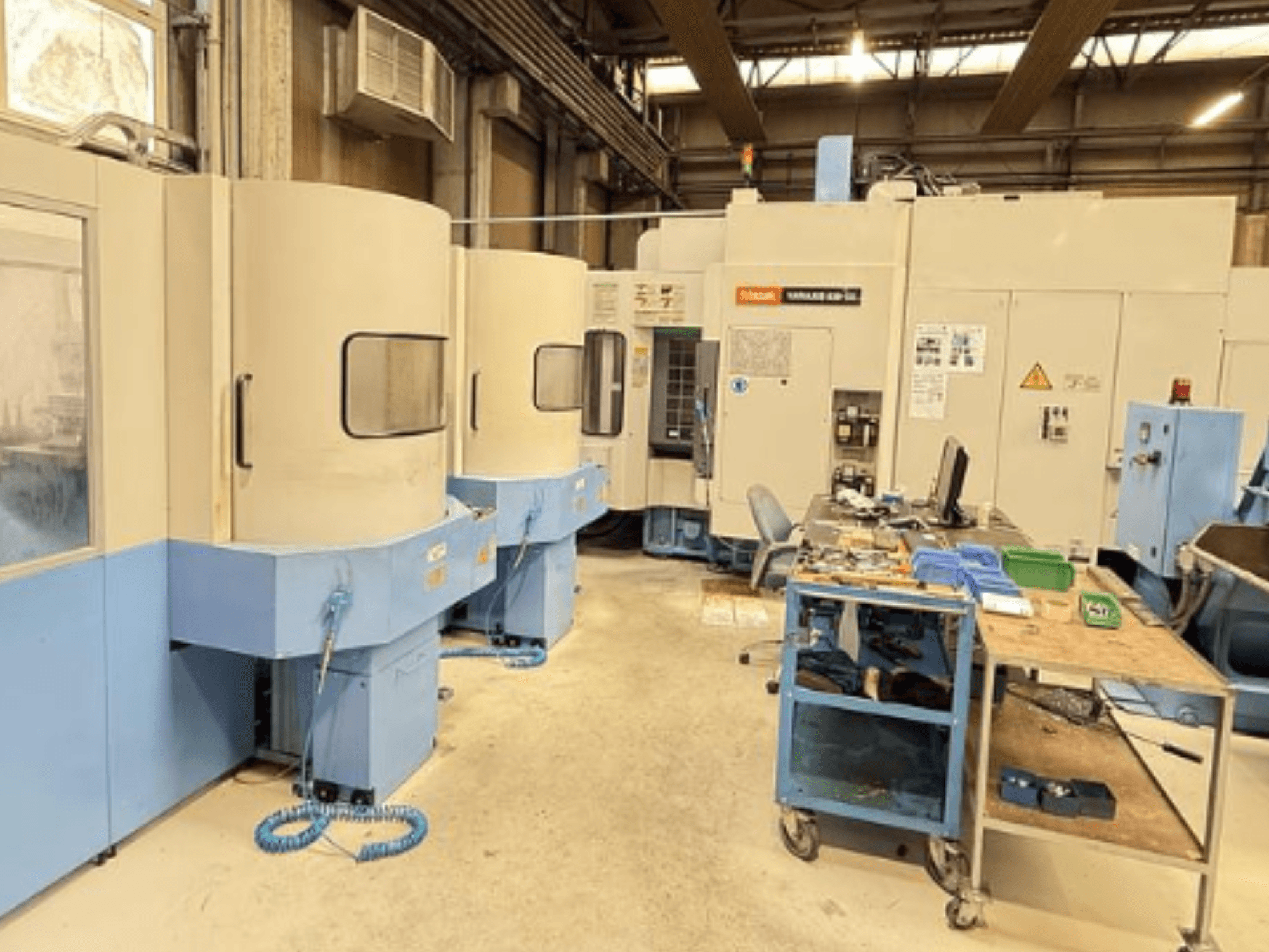 Centro de maquinação vertical Mazak Variaxis 630-5X numa oficina, vista frontal mostrando o painel de controlo e a área de armazenamento de ferramentas.