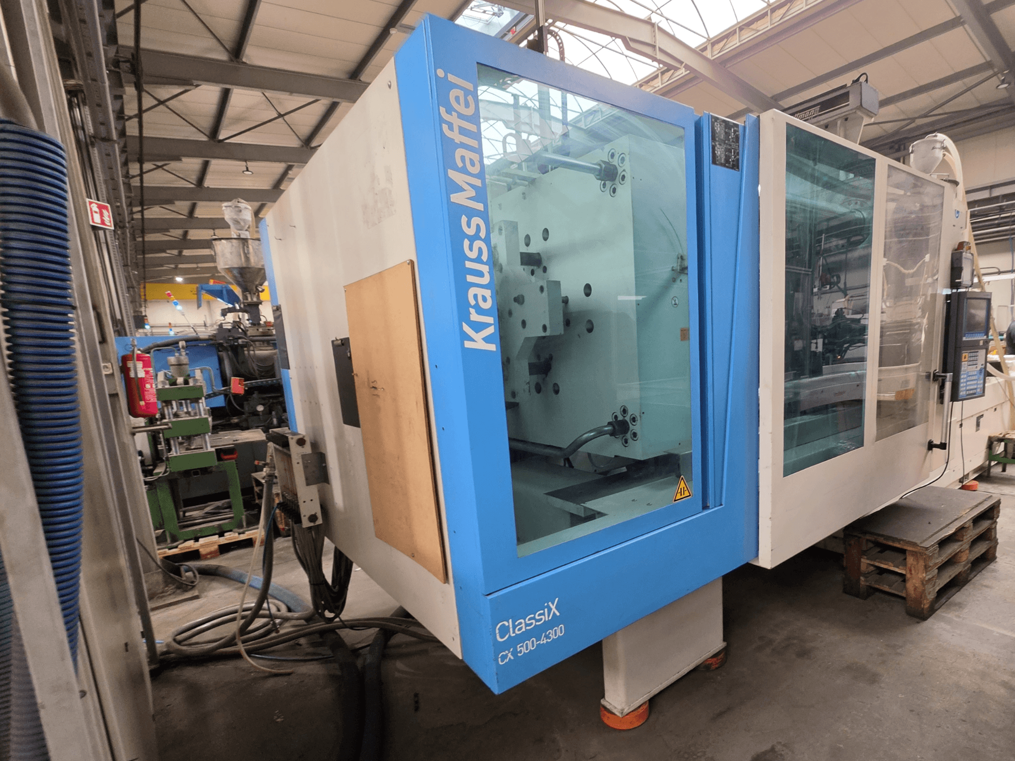 Máquina de moldagem por injeção hidráulica Krauss Maffei 500-4300 CX, vista lateral, mostrando o painel de controlo e os componentes operacionais.