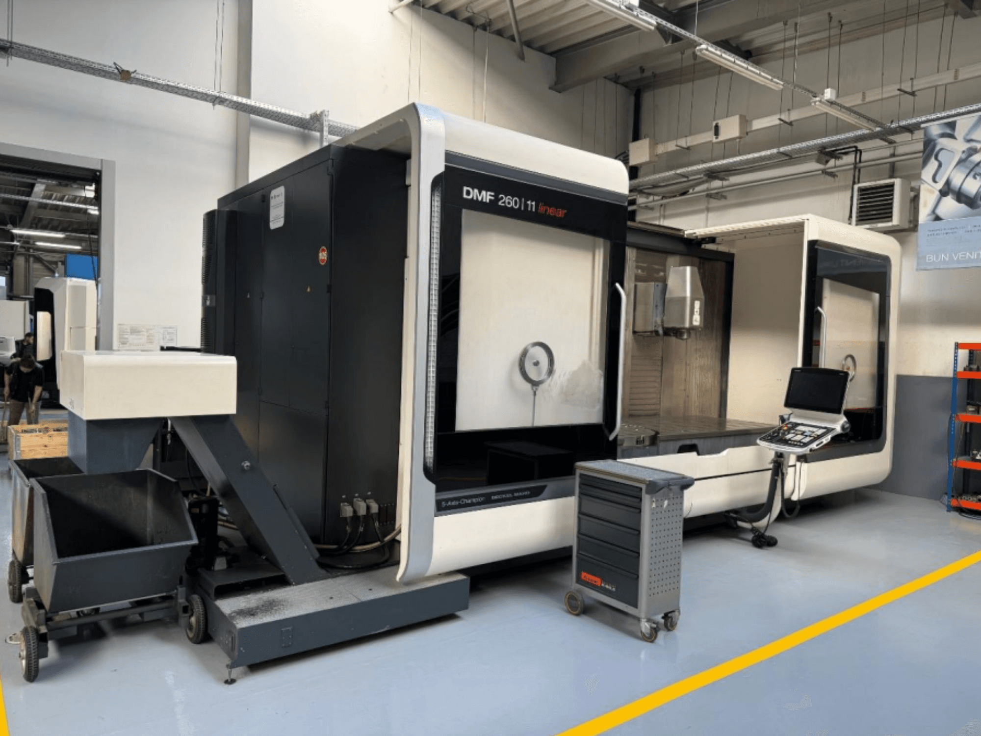 Fresadora linear DMG MORI DMF 260 vista de frente, com um painel de controlo de ferramentas e um carrinho de ferramentas móvel nas proximidades.