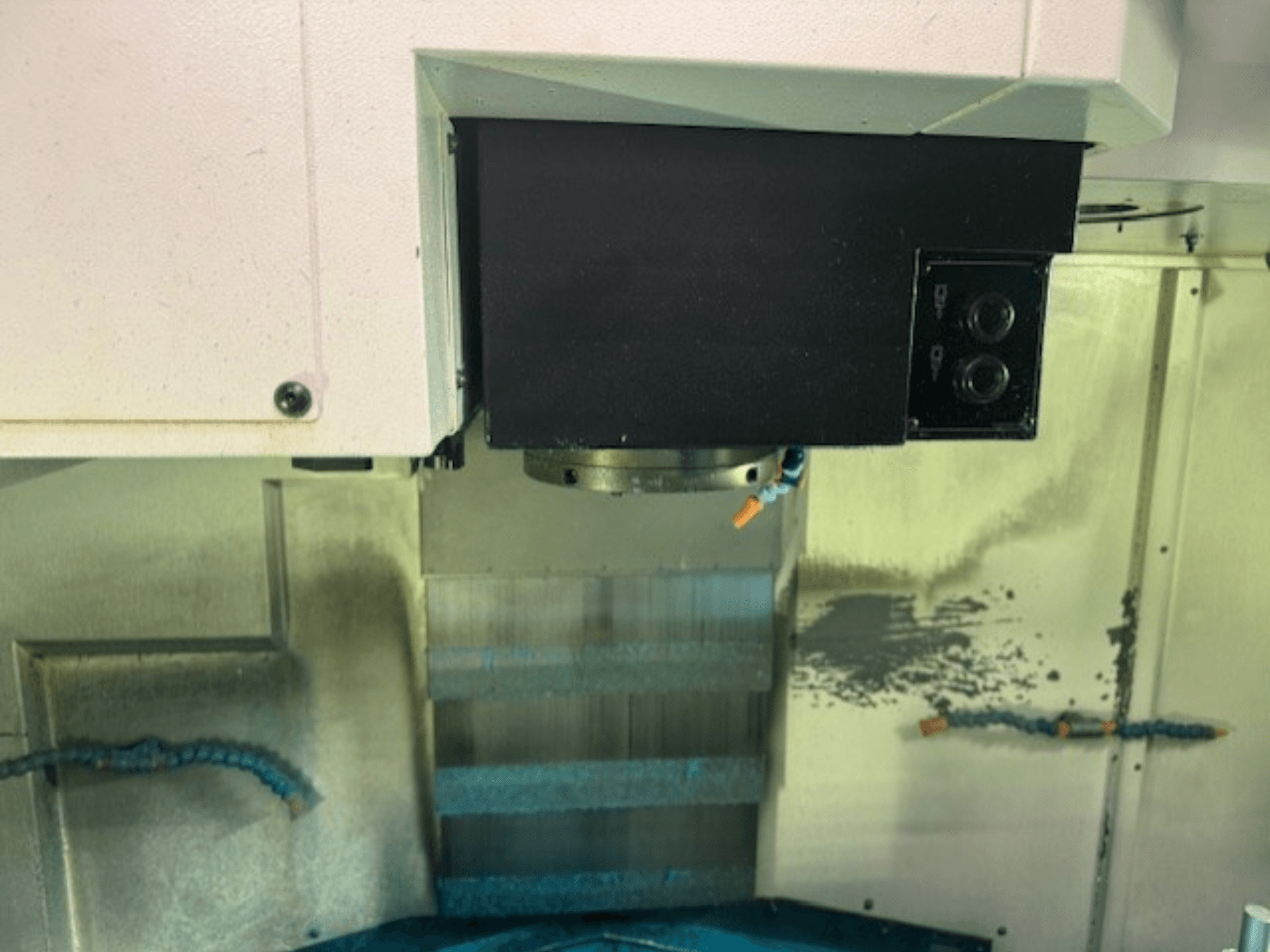 Grande plano de um painel de controlo de uma fresadora CNC e de um suporte de ferramentas, mostrando detalhes da marca, botões e superfície de trabalho.