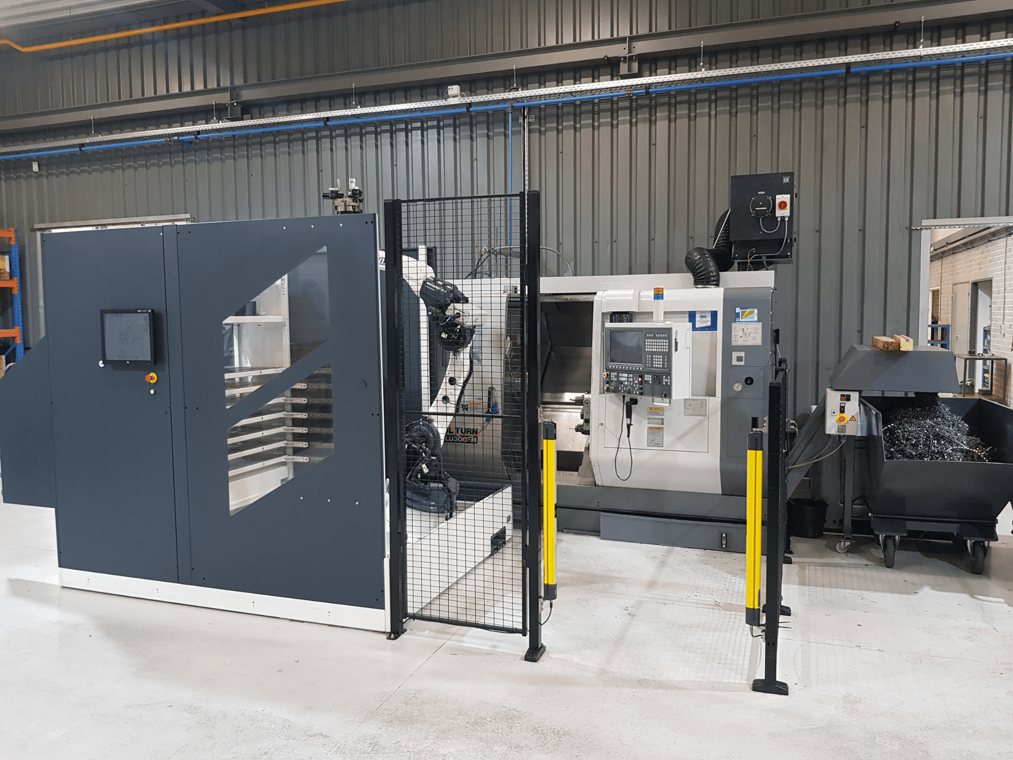 Torno automático ALTURN e máquina CNC mostrados numa configuração de fábrica; vista frontal com painel de controlo e vedação de segurança visível.