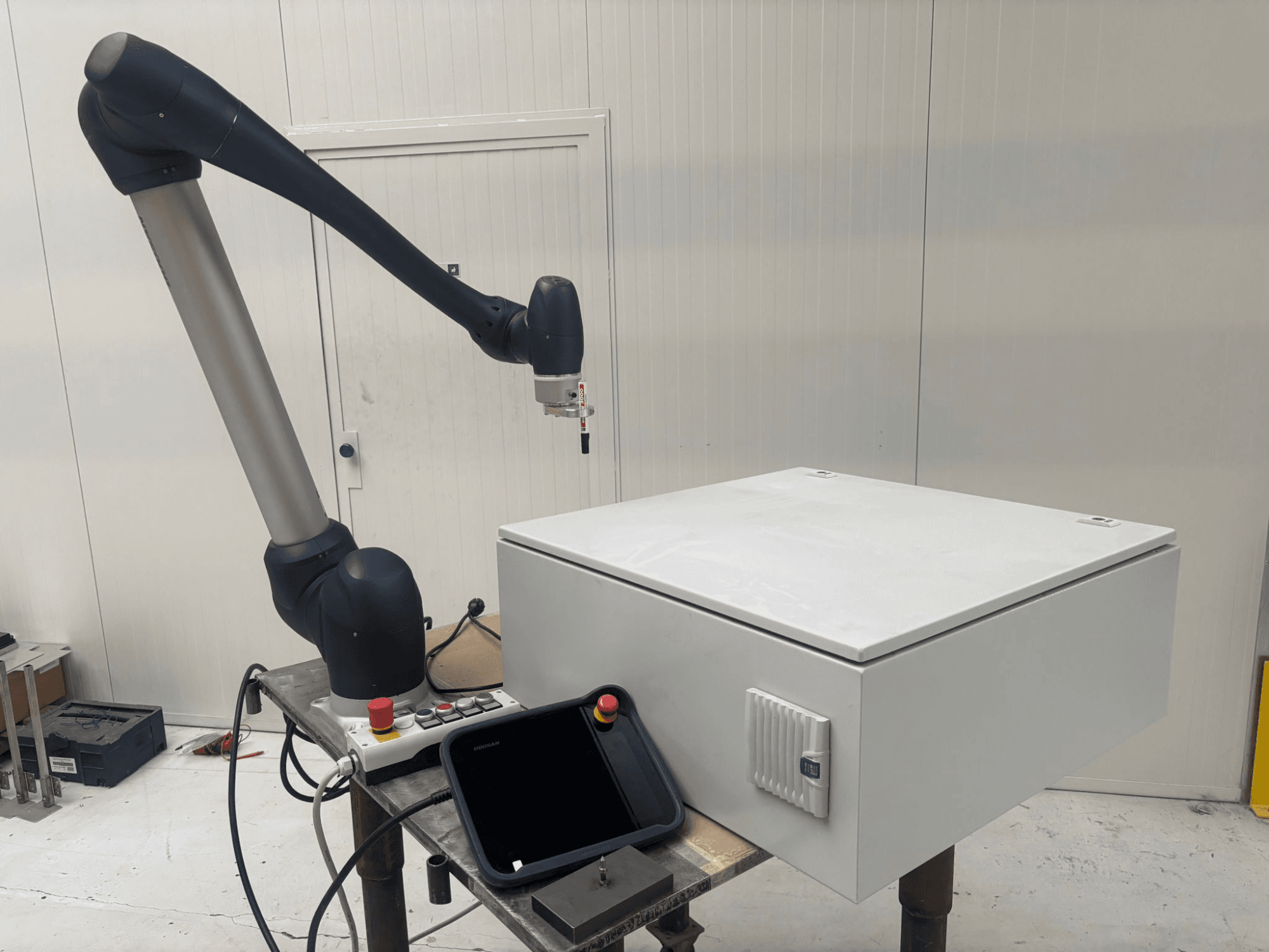 Robô colaborativo DOOSAN M0617 em vista lateral, com o braço robótico estendido sobre uma interface de controlo e uma caixa branca sobre uma mesa.