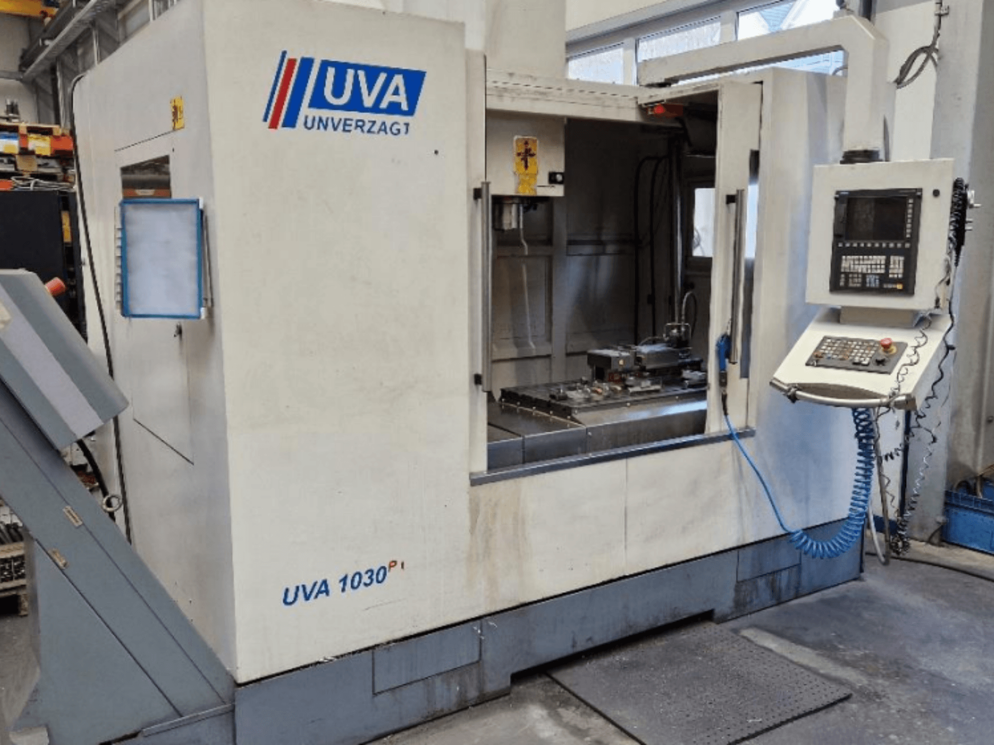 Máquina-ferramenta UVA 1030P numa oficina, vista frontal mostrando o painel de controlo, a área de trabalho e a superfície de corte limpa.
