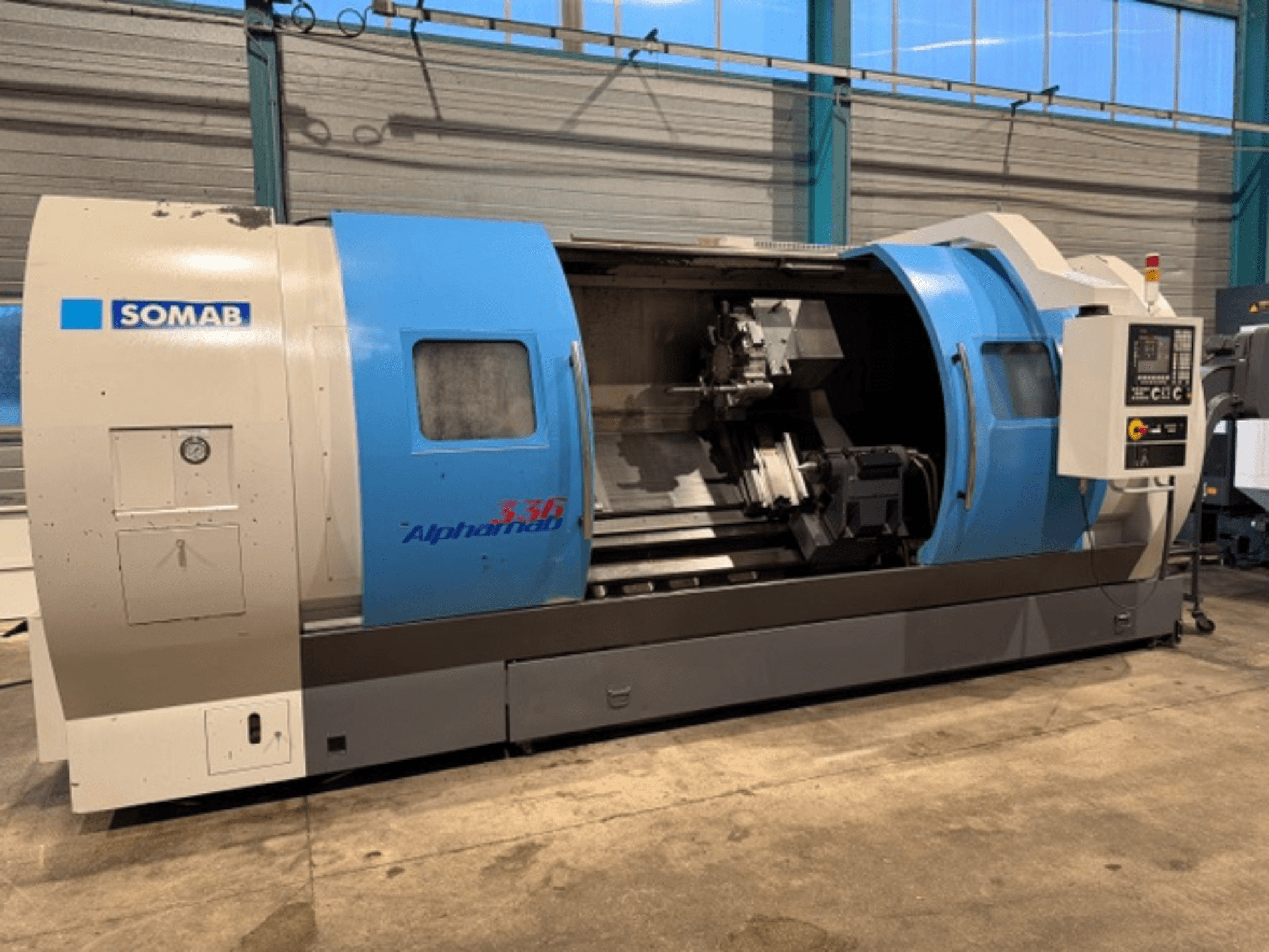 Torno CNC SOMAB Alpha 336, vista frontal, com caixa azul e cinzenta e um painel de controlo lateral para a operação.