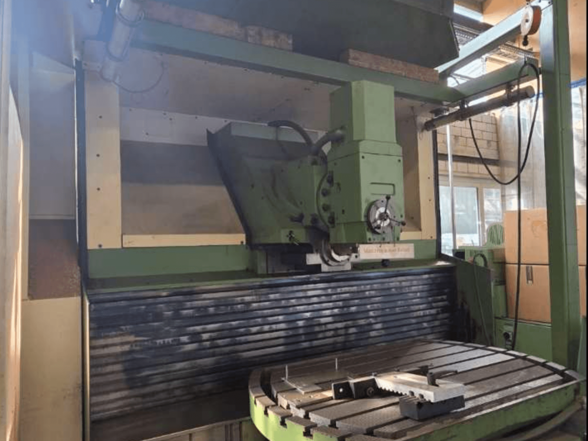 Centro de Maquinação Universal MAHO MH1000 C em vista frontal, mostrando a estrutura verde, o fuso e a mesa rotativa com uma peça de trabalho.