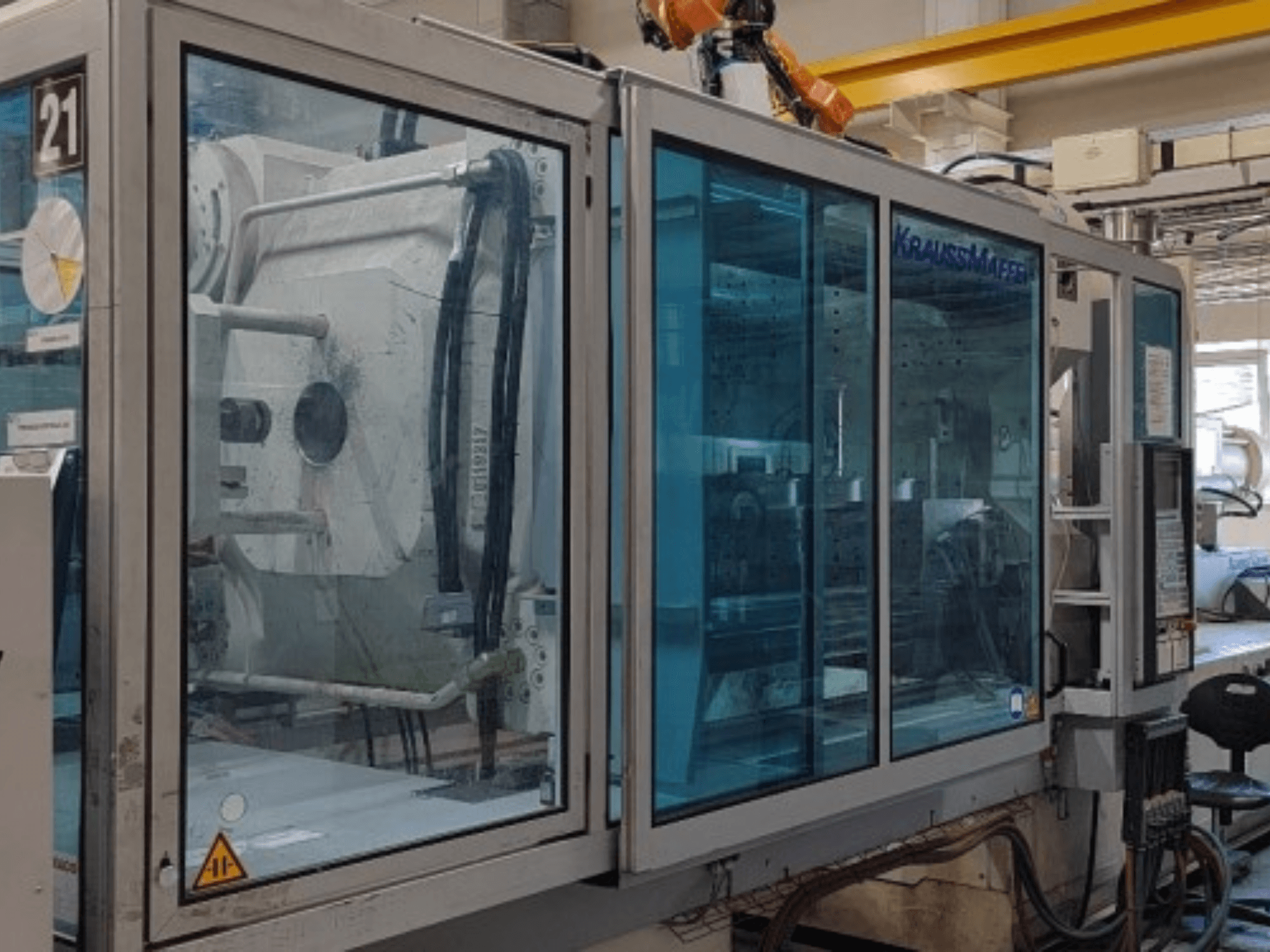 Máquina de moldagem por injeção hidráulica Krauss Maffei KM 575-2700 C2, vista lateral, com painéis de segurança transparentes e painel de controlo.