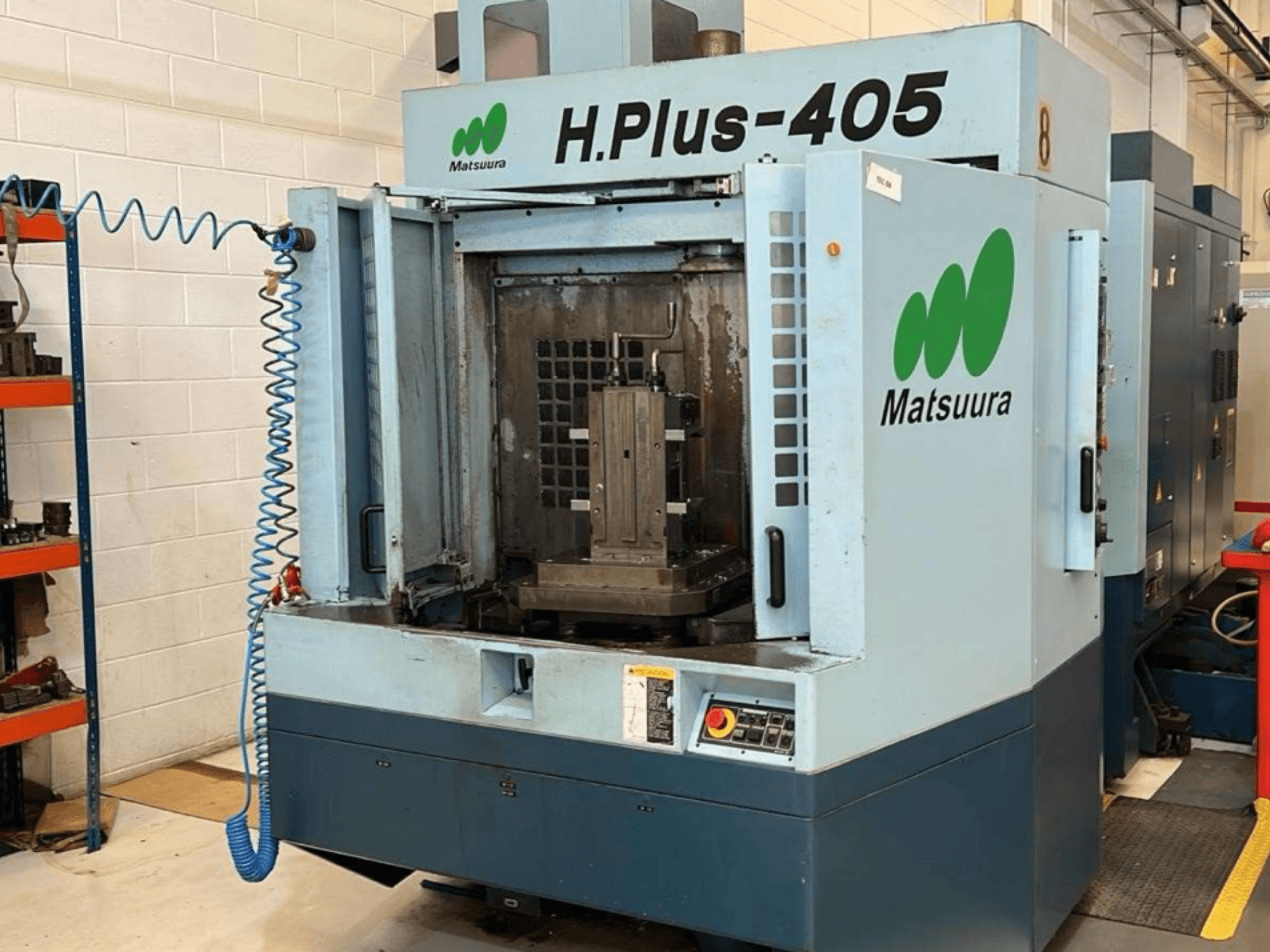 Vista frontal de um centro de maquinagem horizontal Matsuura H.Plus 405 com a porta aberta, mostrando a área de trabalho e o painel de controlo.