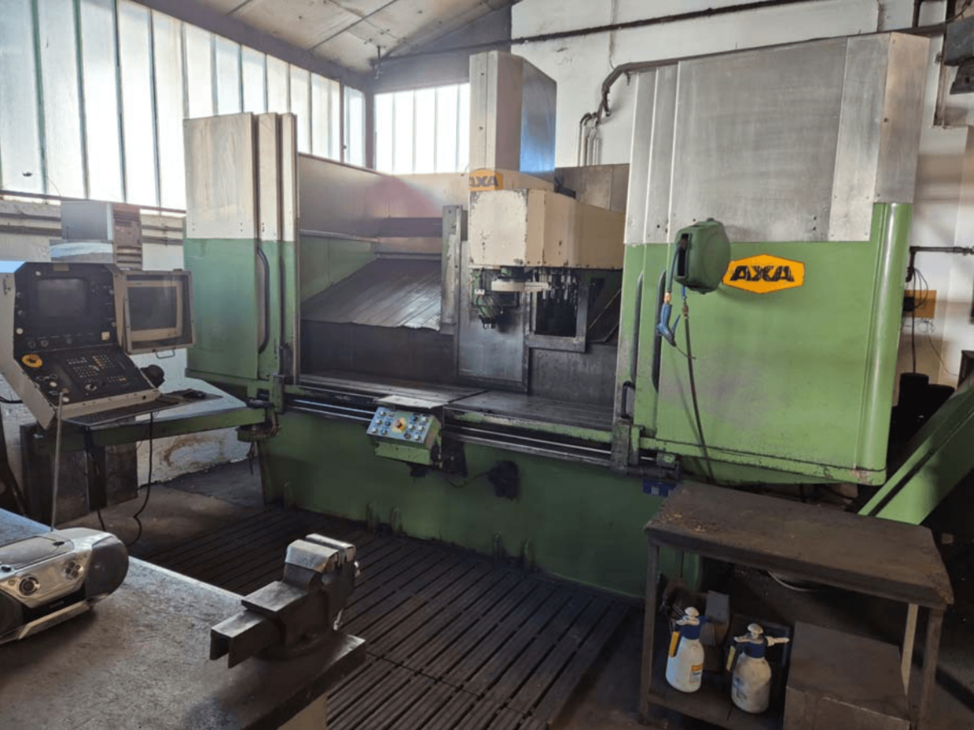 Centro de maquinação vertical AXA VSC-2M, vista frontal, com painel de controlo e área de trabalho com ferramentas de corte e material de limpeza.