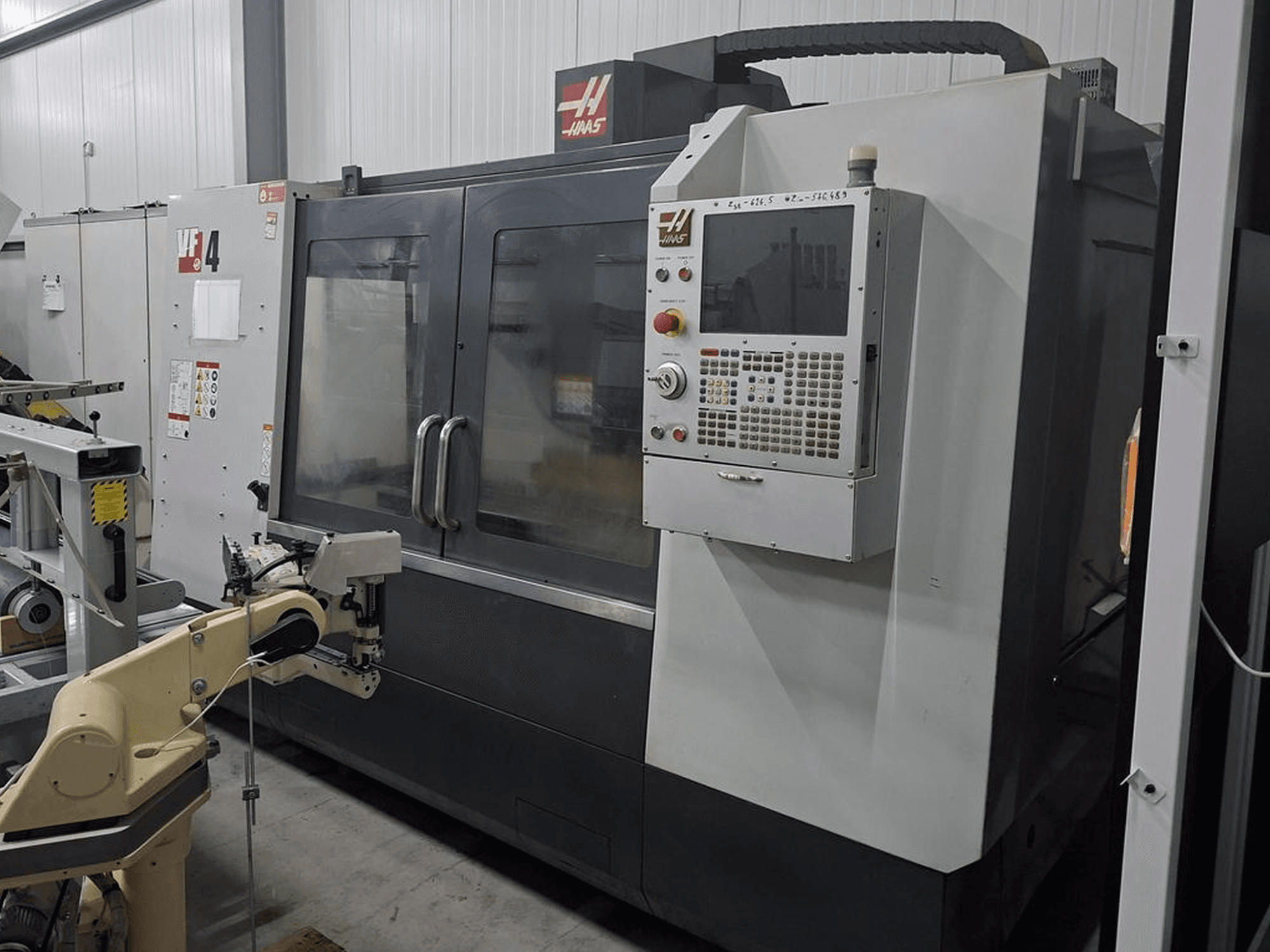 Fresadora CNC Haas VF-4 em vista frontal, com um painel de controlo numérico e braço robótico para automação.