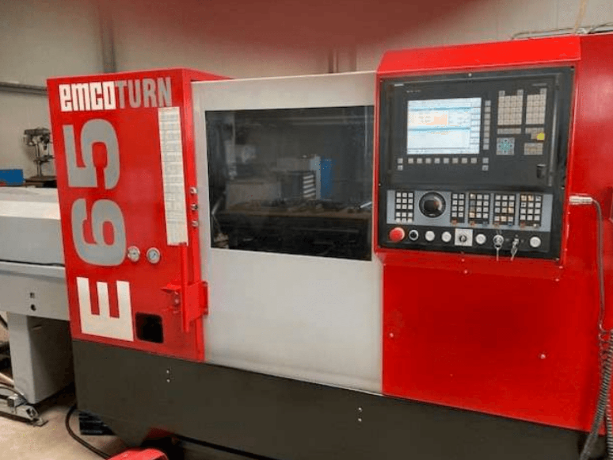 Torno CNC EMCO Turn E65, vista frontal mostrando o painel de controlo, o ecrã grande e a área de trabalho atrás do vidro.