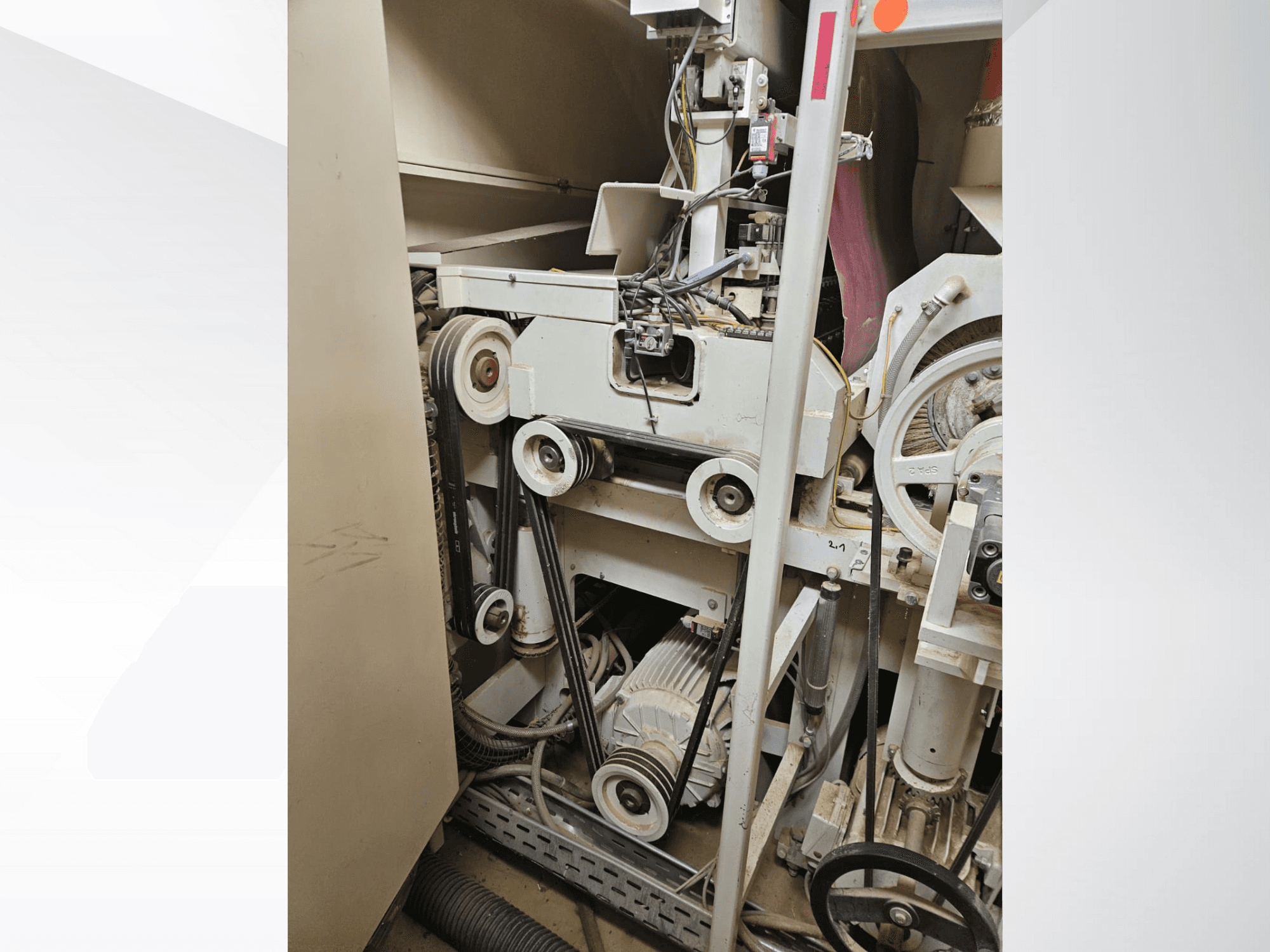 Interior de máquina industrial com correias e polias, com um motor e cablagem, visto de lado.