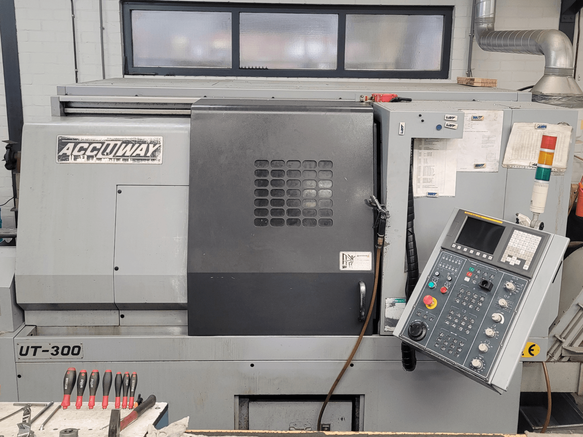 Máquina CNC Accuway UT-300 em vista frontal, com um painel de controlo e vários botões operacionais, numa oficina.
