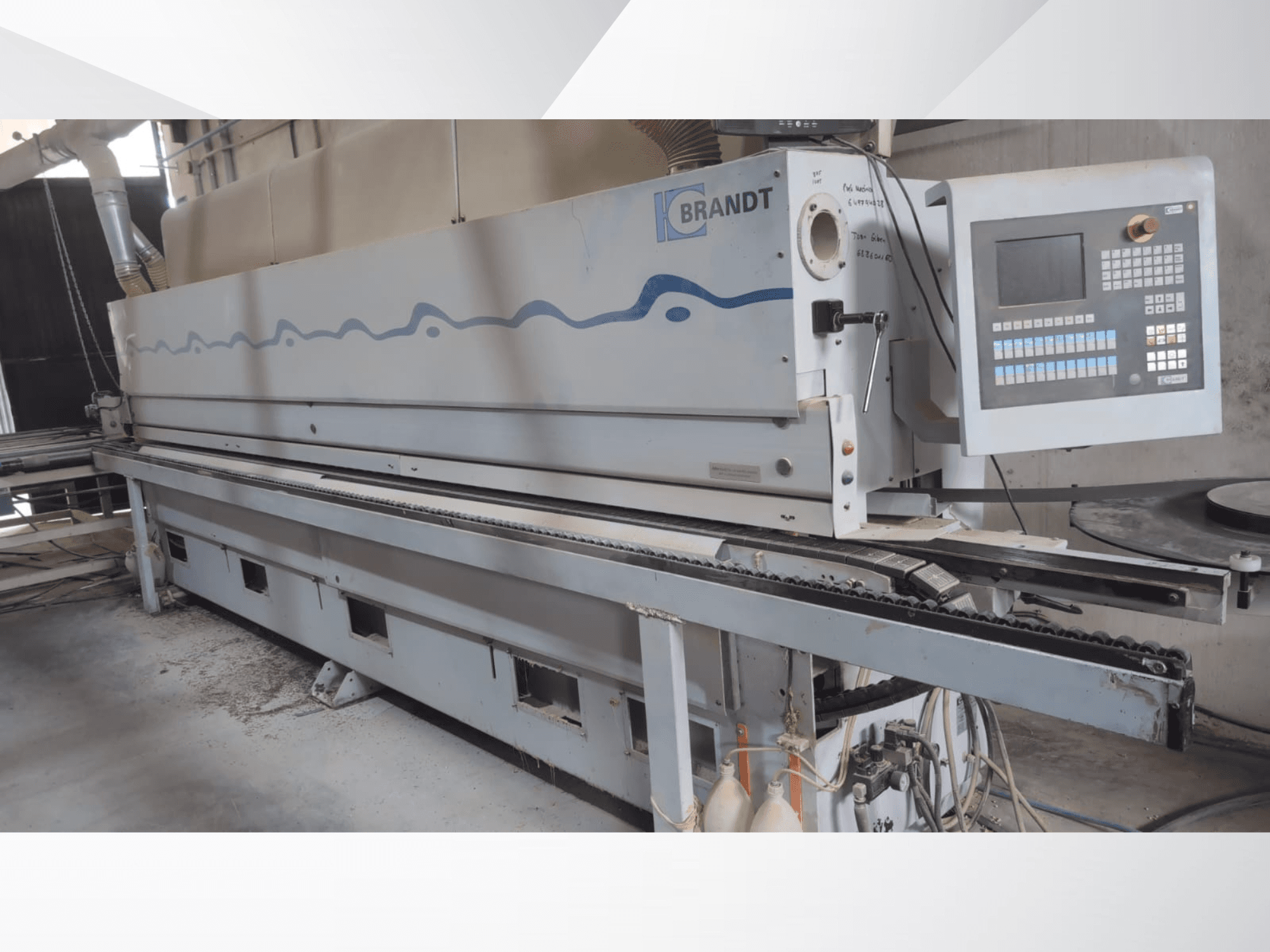 Máquina de colar bordas BRANDT KDF 560 vista de frente, com o painel de controlo e o transportador de alimentação, apresentando resíduos de pó visíveis no chão.