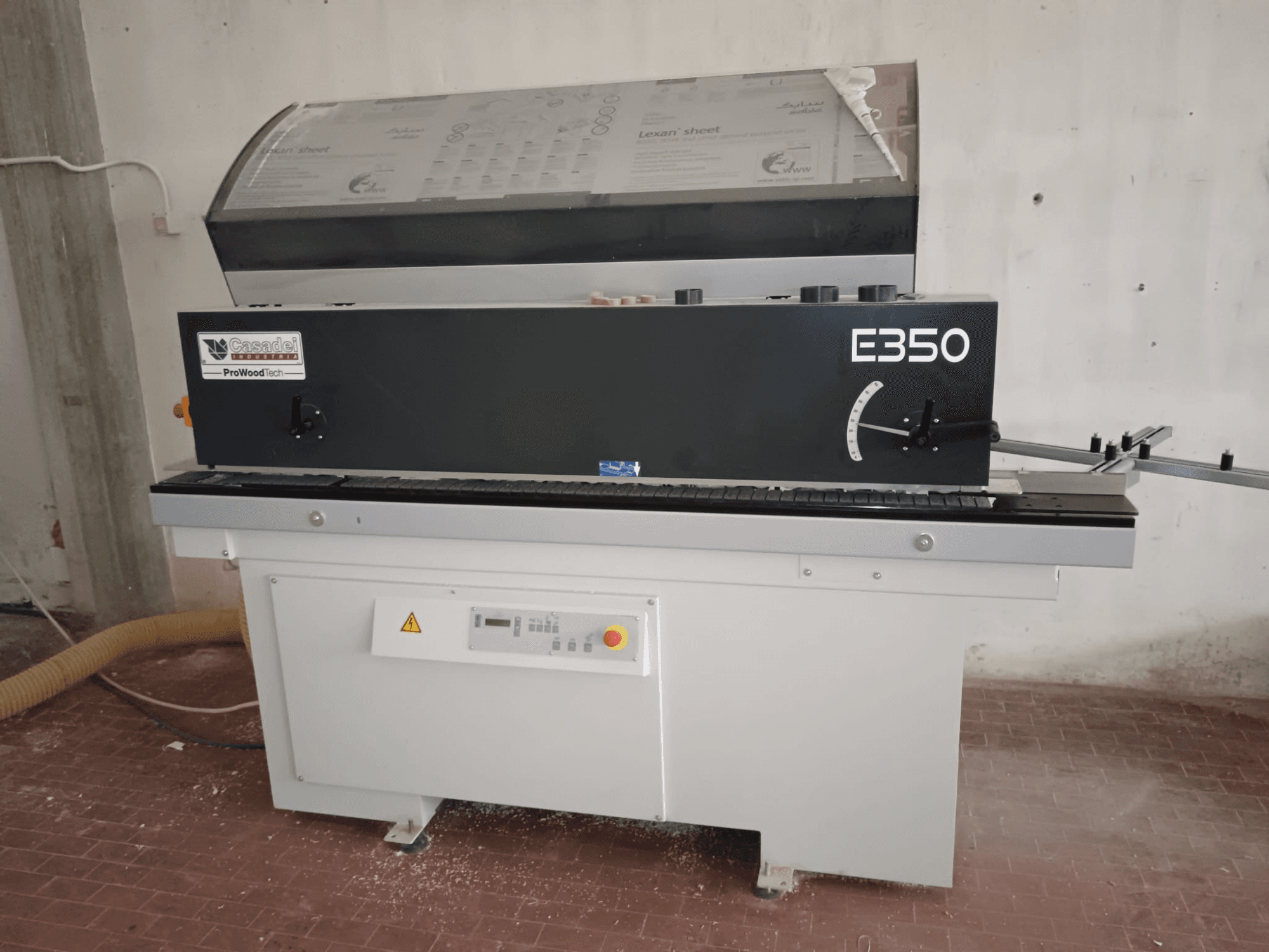 Cesaroli ProWoodtech E350, vista lateral de uma máquina para trabalhar madeira com painel de controlo e acumulação de pó, montada numa base branca.