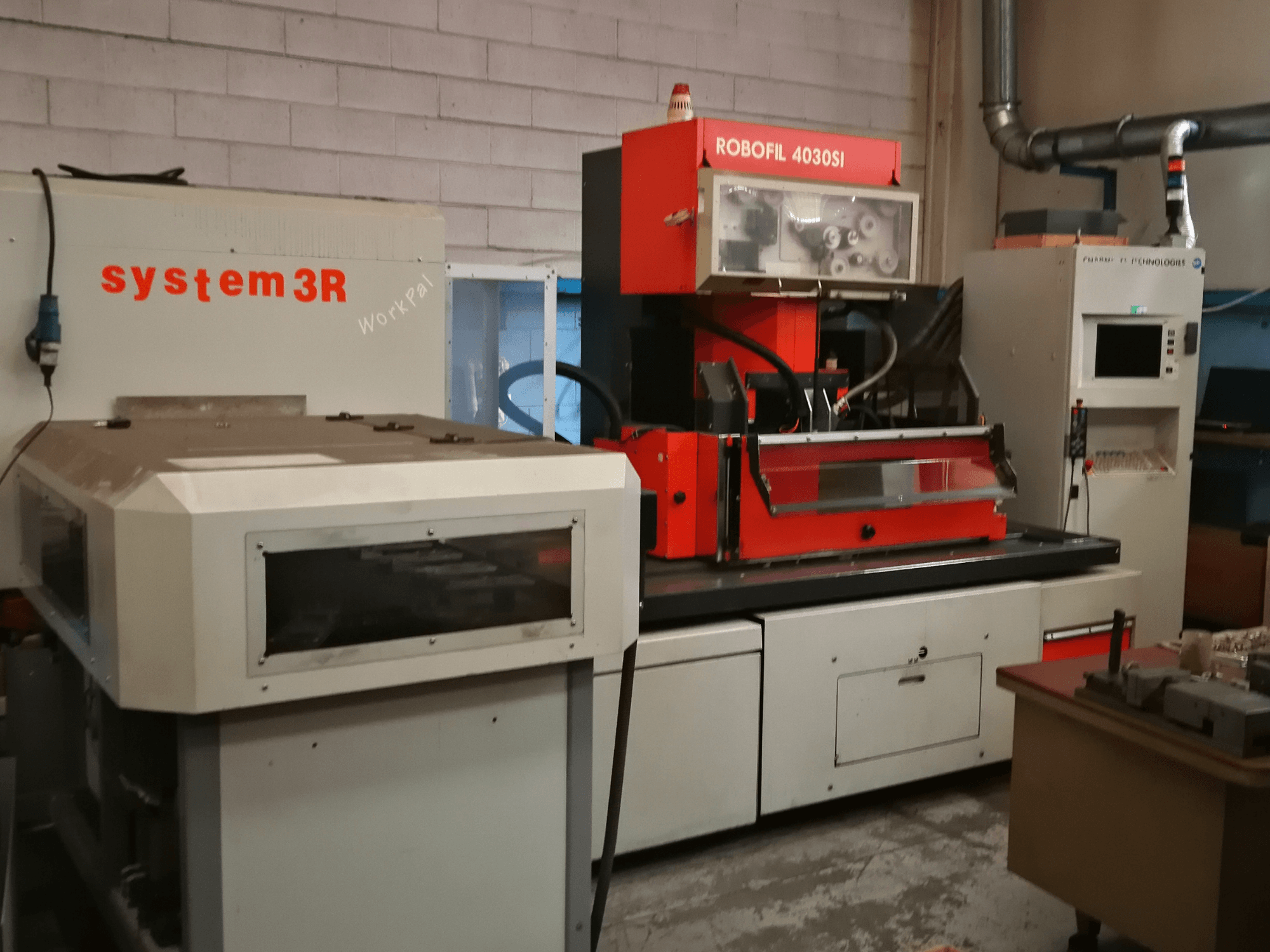 Vista frontal da máquina de electroerosão por fio CHARMILLES ROBOFIL 4030 Si, com exterior vermelho e cinzento e posto de trabalho system3R adjacente.