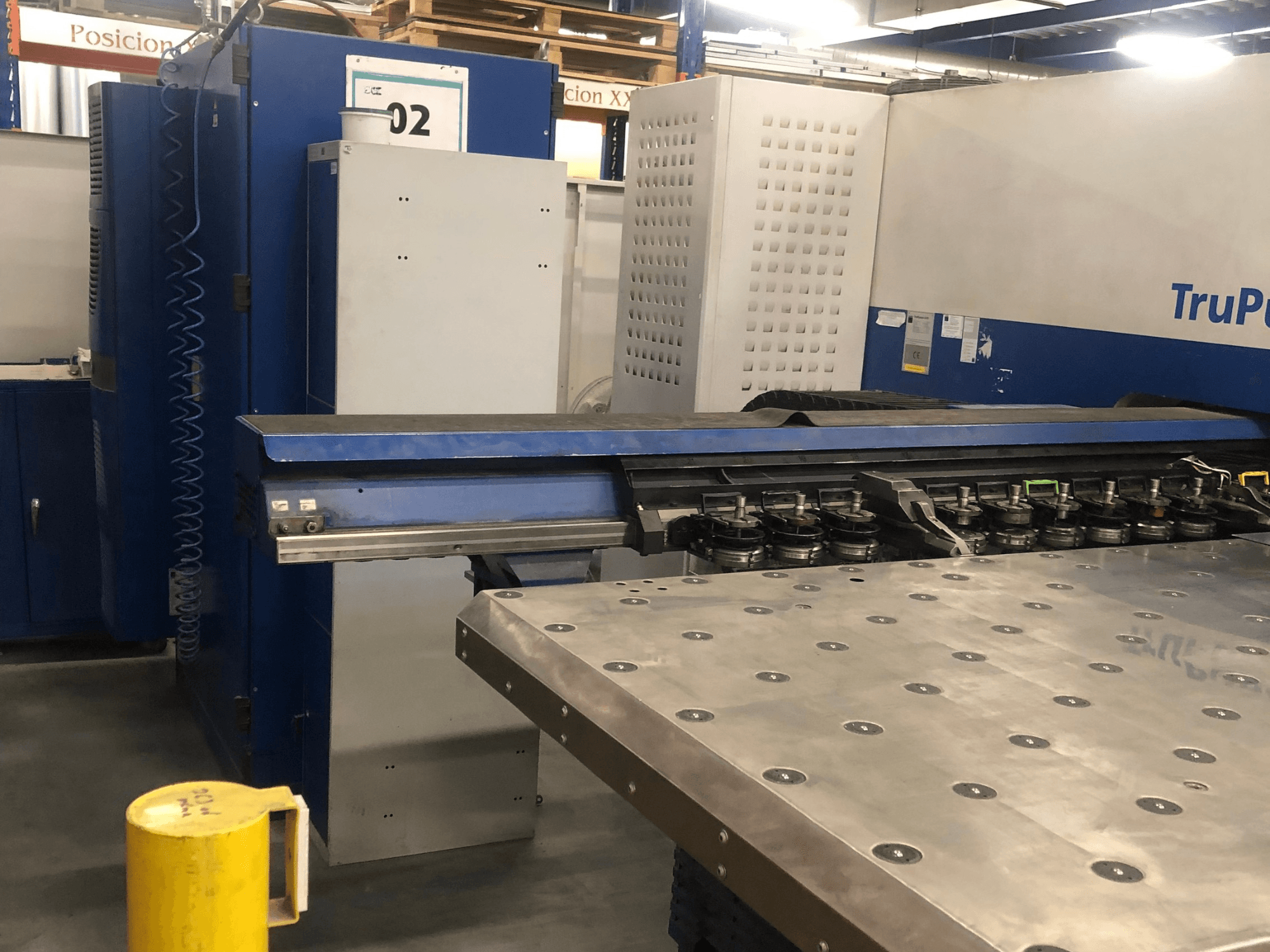 Máquina de perfuração CNC TRUMPF TruPunch 5000, vista frontal que mostra a torre de ferramentas e o painel de controlo, com uma mesa de trabalho metálica nas proximidades.