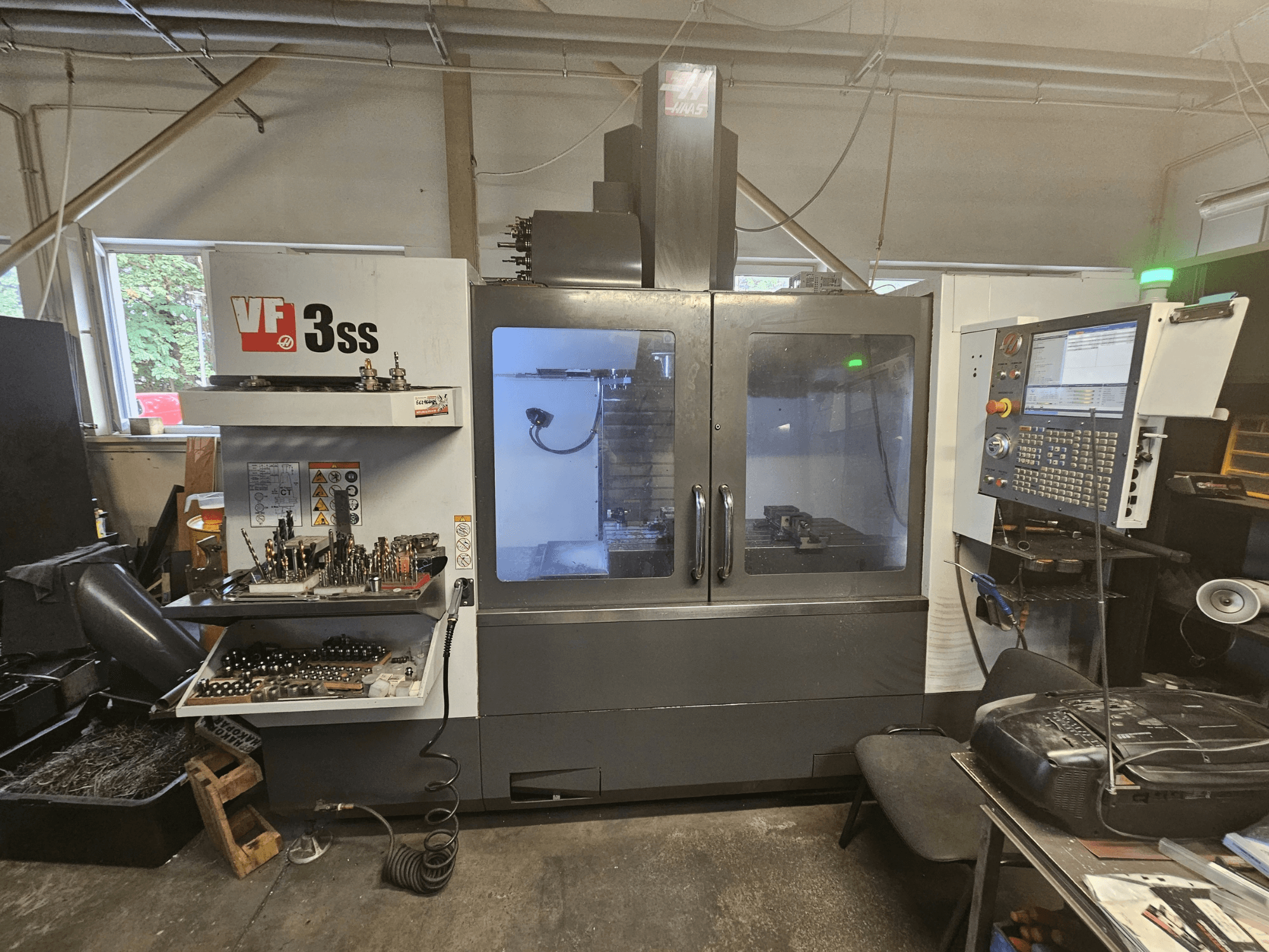 Centro de maquinagem vertical Haas VF-3SS numa oficina, vista frontal que mostra o painel de controlo e o compartimento de armazenamento de ferramentas.
