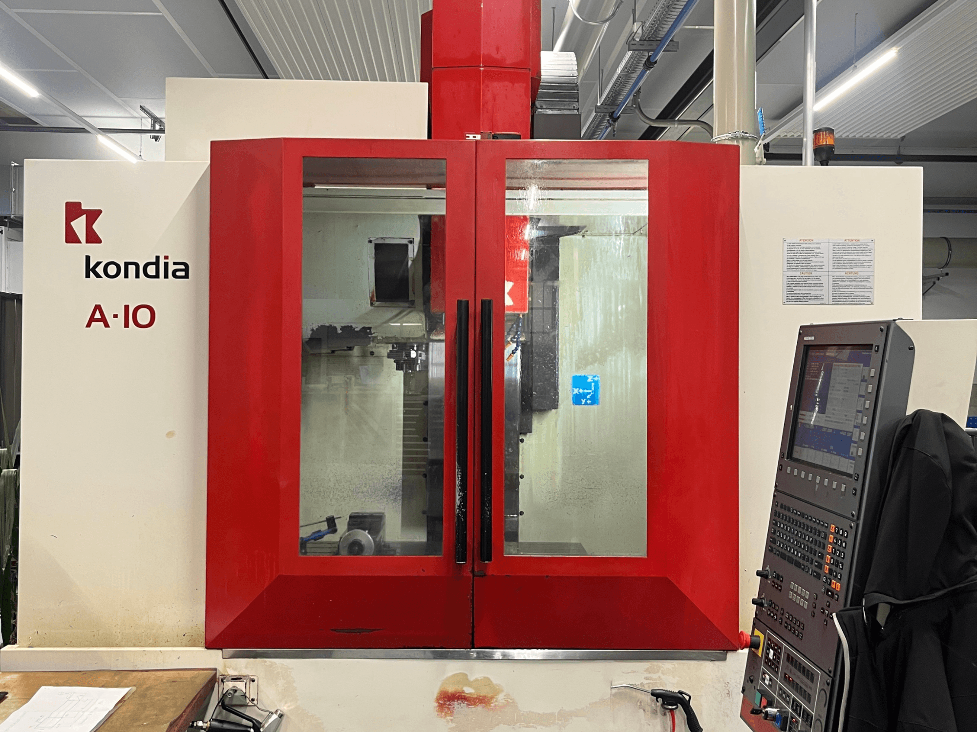 Centro de maquinação vertical KONDIA A10, vista frontal; apresenta portas de vidro vermelhas e painel de controlo à direita.