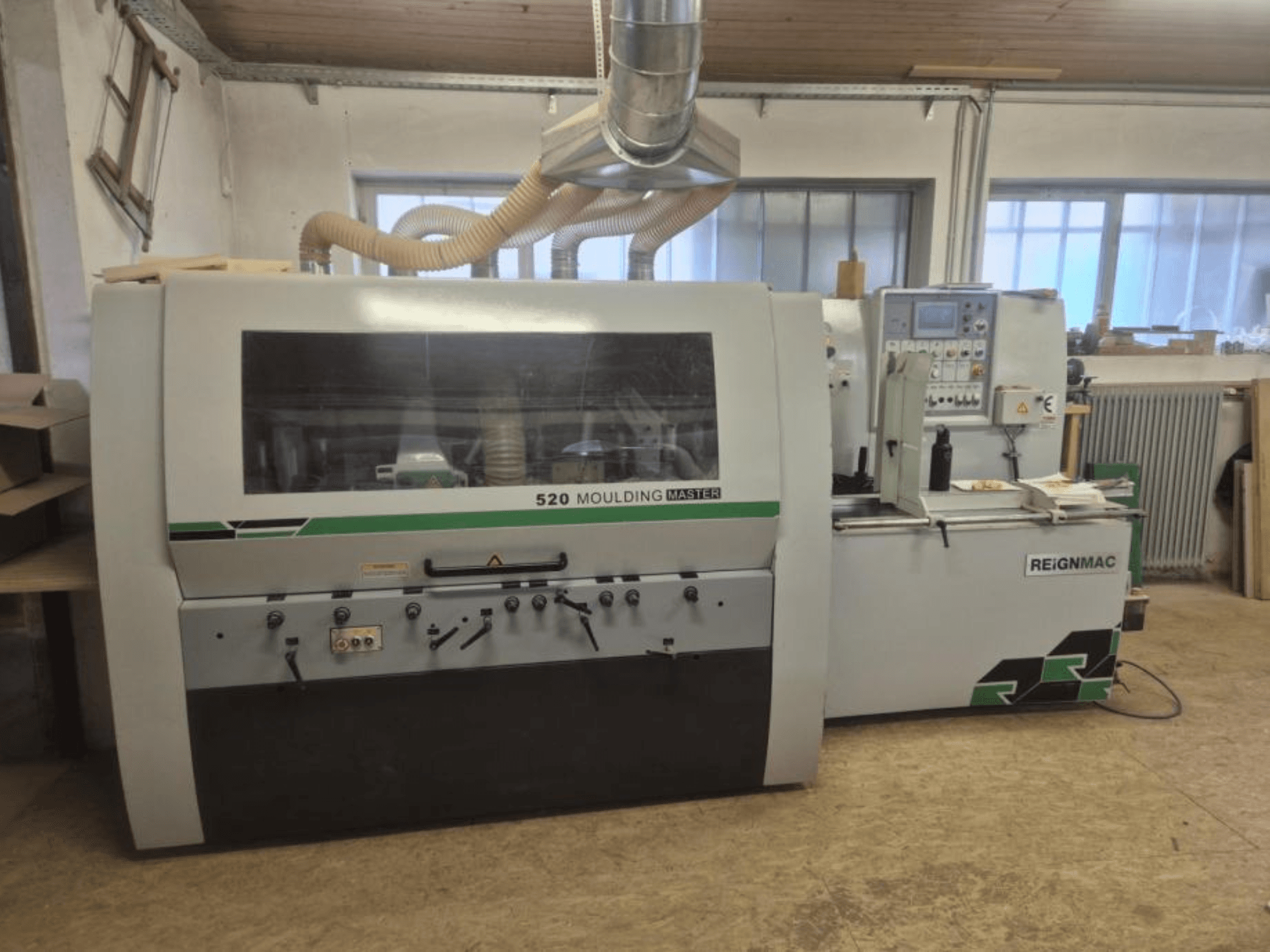 Vista frontal da plaina para madeira REIGNMAC 520 MOULDING MASTER, mostrando o painel de controlo, os rolos de alimentação e o sistema de extração de poeiras.